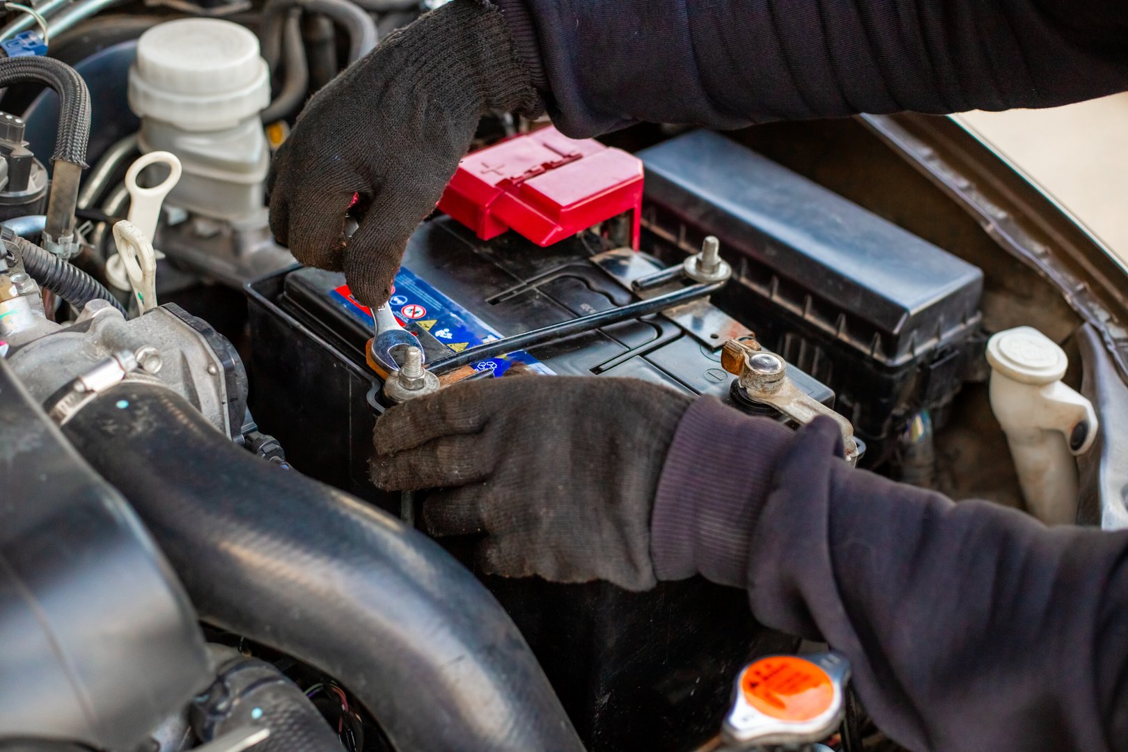 Replacing a car battery. The mechanic installs the battery, securing the battery mounting bracket with a wrench.