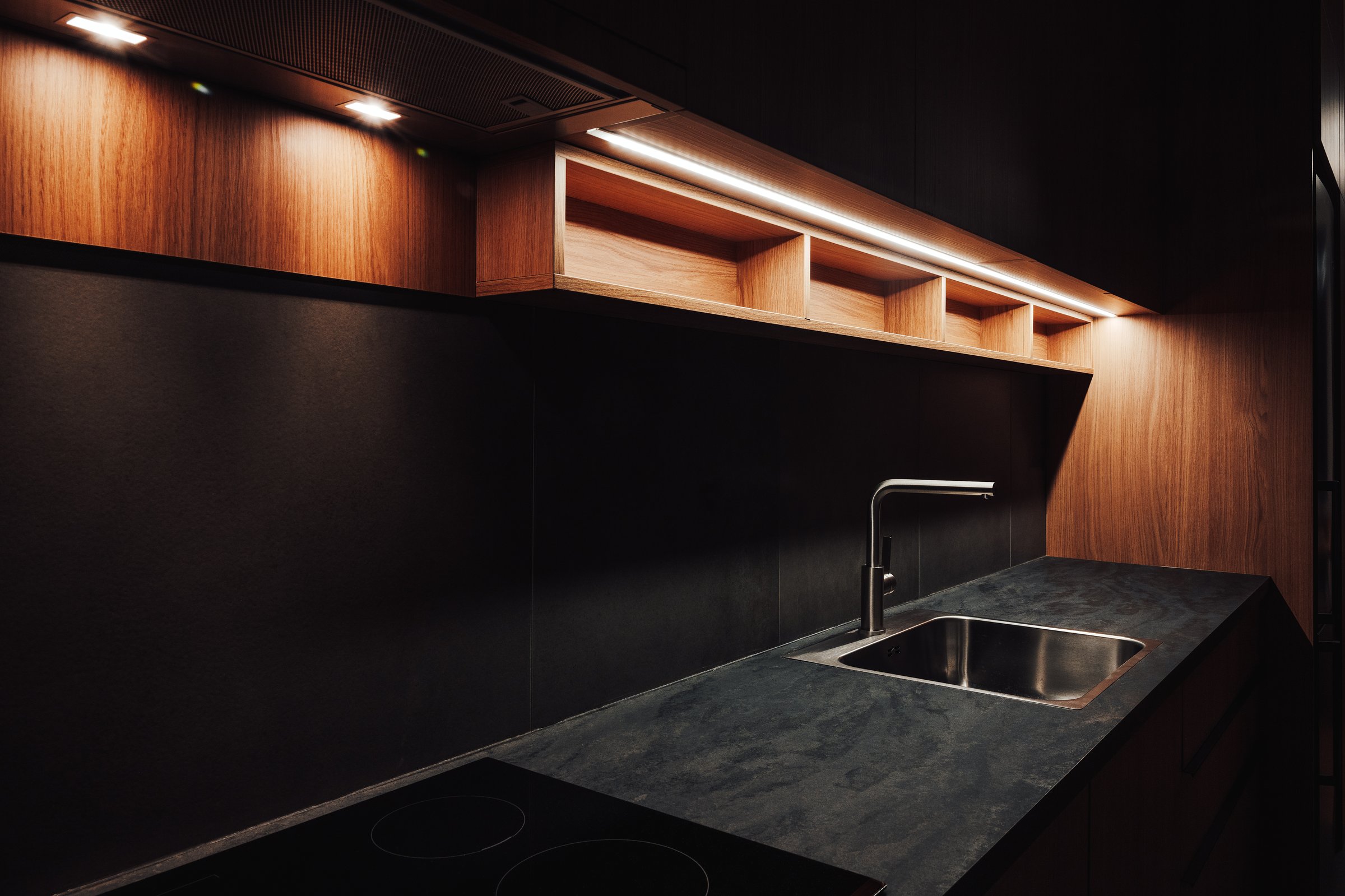 Water faucet and metallic sink in modern sleek kitchen with led strip light, selective focus