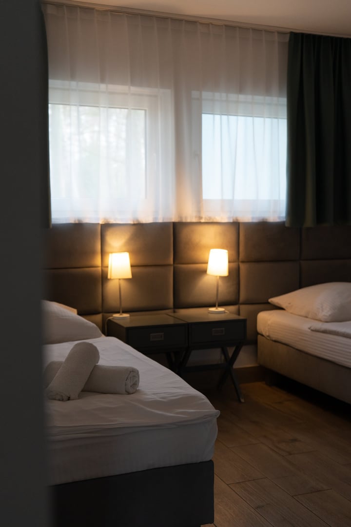 Cozy twin bedroom with two neatly made beds, rolled towels, and soft warm lighting from bedside lamps. Calm and relaxing interior with wooden floor and minimal decor, perfect for illustrating hospitality, hotel design, or home comfort concepts.