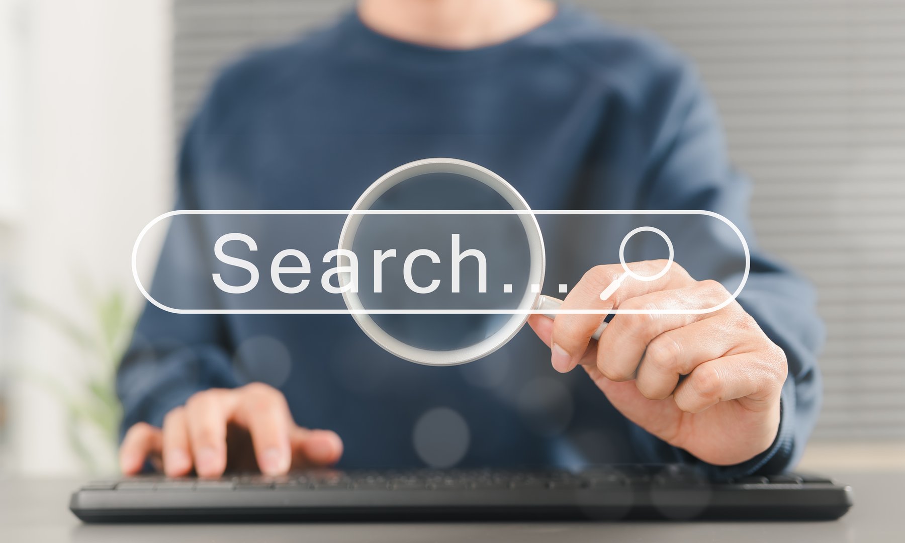 SEO search engine optimization concept. Person uses keyboard while holding magnifying glass with search bar labeled Search, online search engine optimization, and digital marketing strategies.