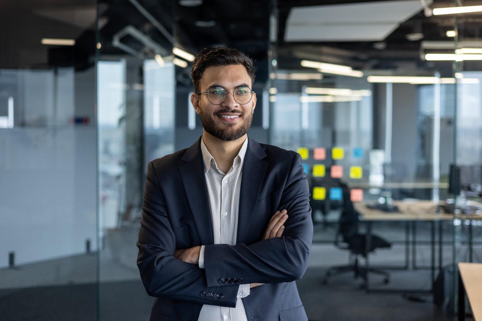A professional businessman standing confidently in a modern office setting with glass walls and bright lighting, exuding positivity and success.