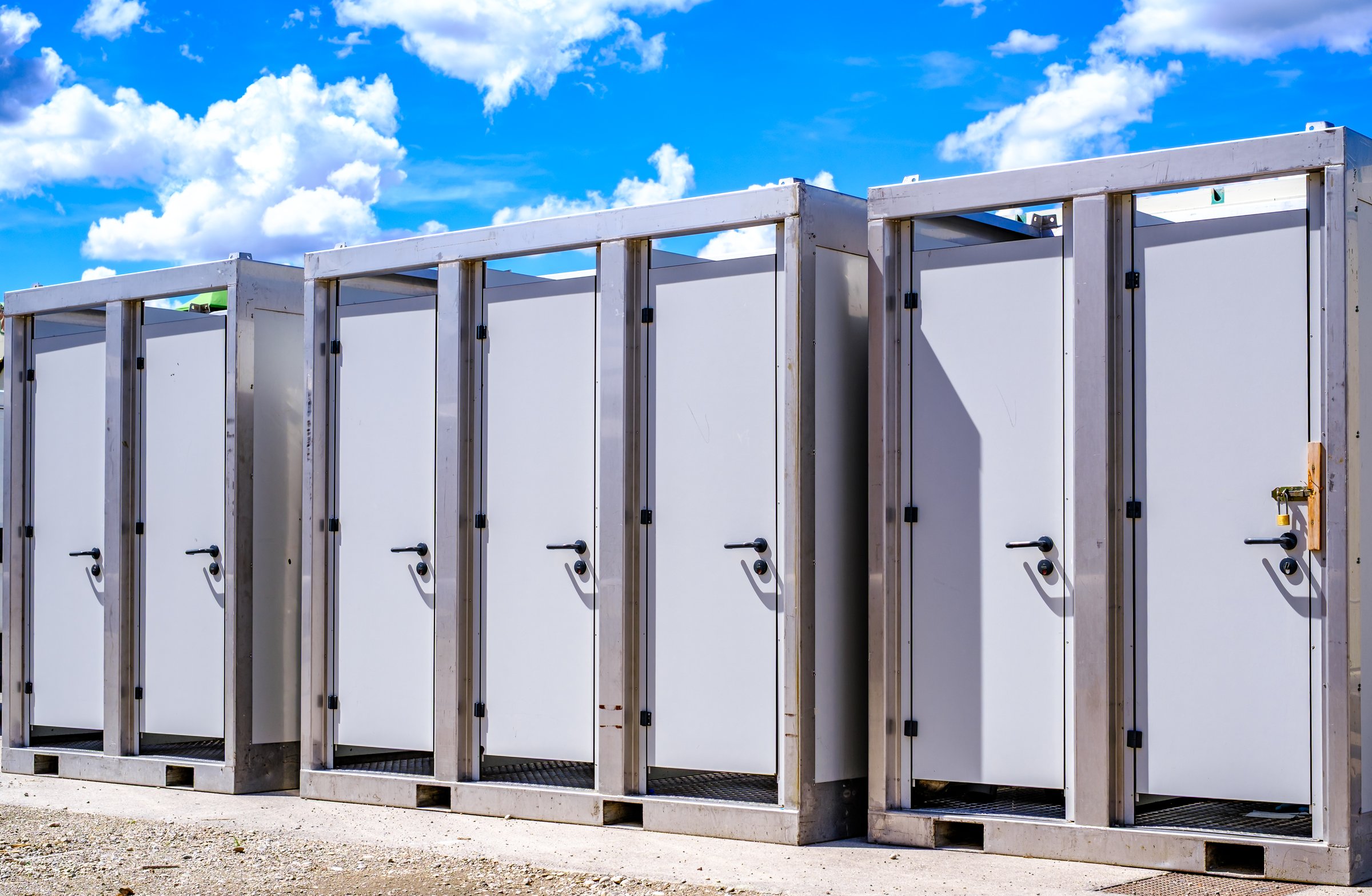 Multiple portable restrooms arranged in a row at a construction site provide convenient facilities for workers during daylight hours in a spacious outdoor setting.