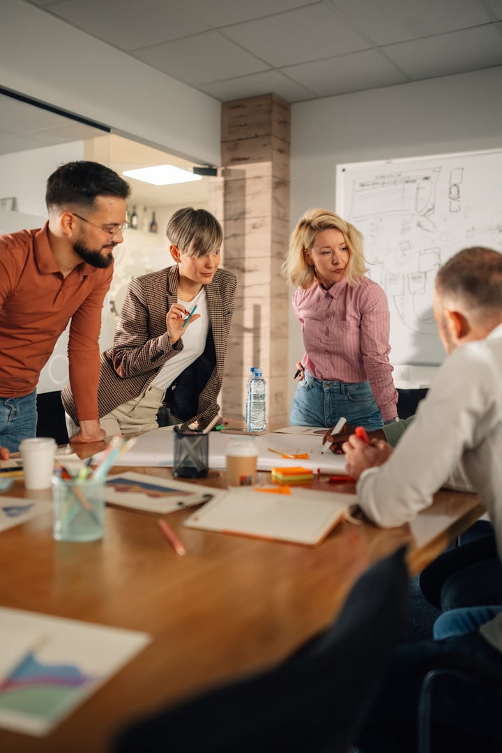 Four marketing professionals are gathered around a table, analyzing charts, discussing ideas, and developing a new strategy during a productive brainstorming session in a modern office