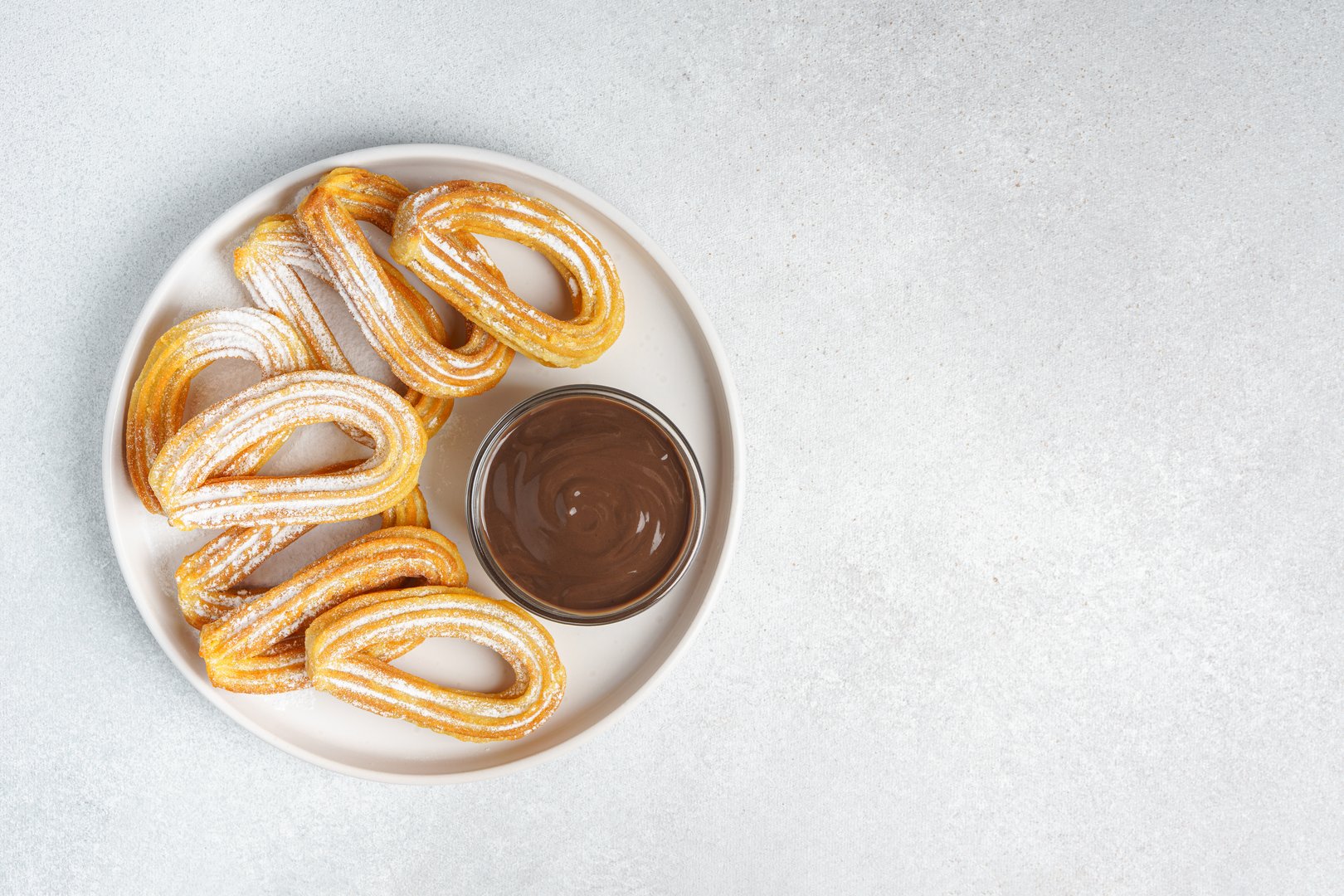 Traditional spanish dessert churros, fried dough pastry dusted with powdered sugar and chocolate sause on white background. Street food, sweet snack, homemade dessert. Top view, copy space
