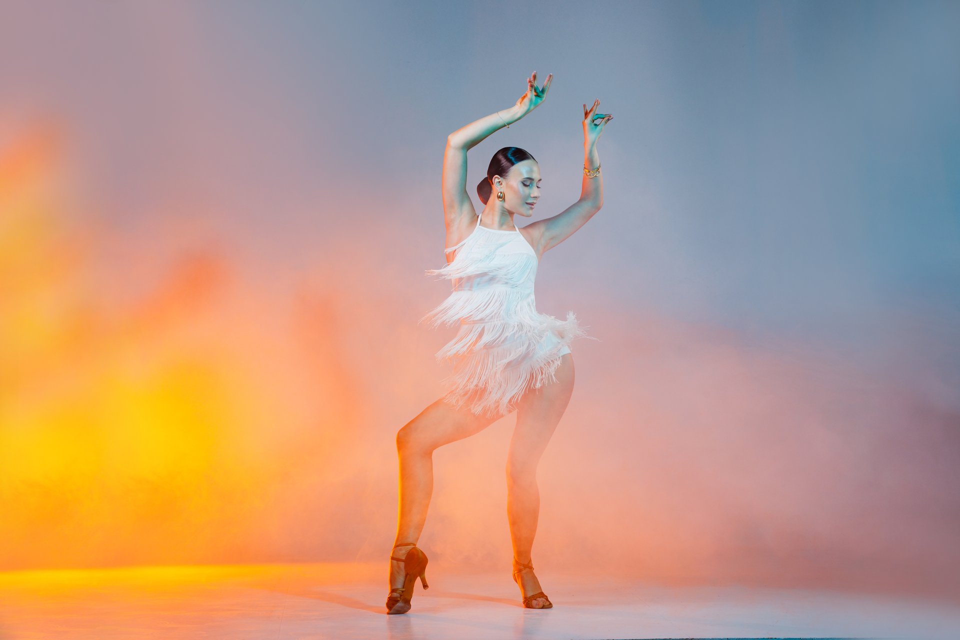 Elegant dancer in fringed dress dancing solo salsa dance showing dramatic pose under artistic lighting