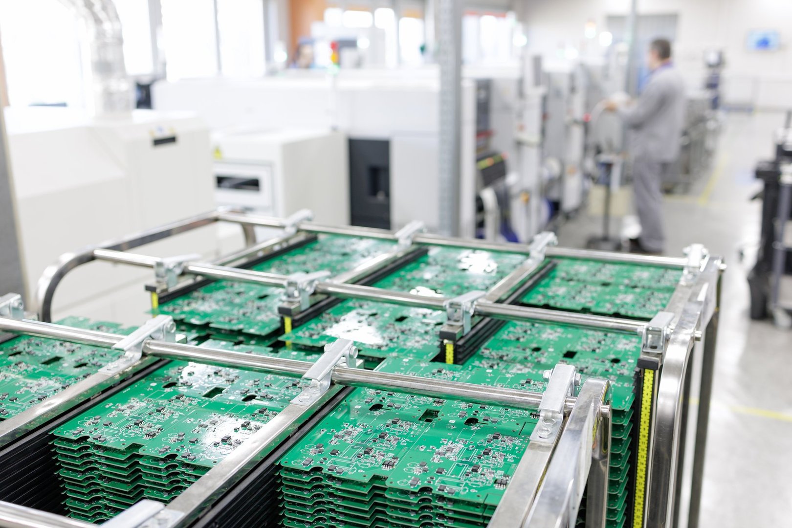Stacked PCB panels in an ESD rack with technician and SMT equipment in the background on a modern automated electronics production line