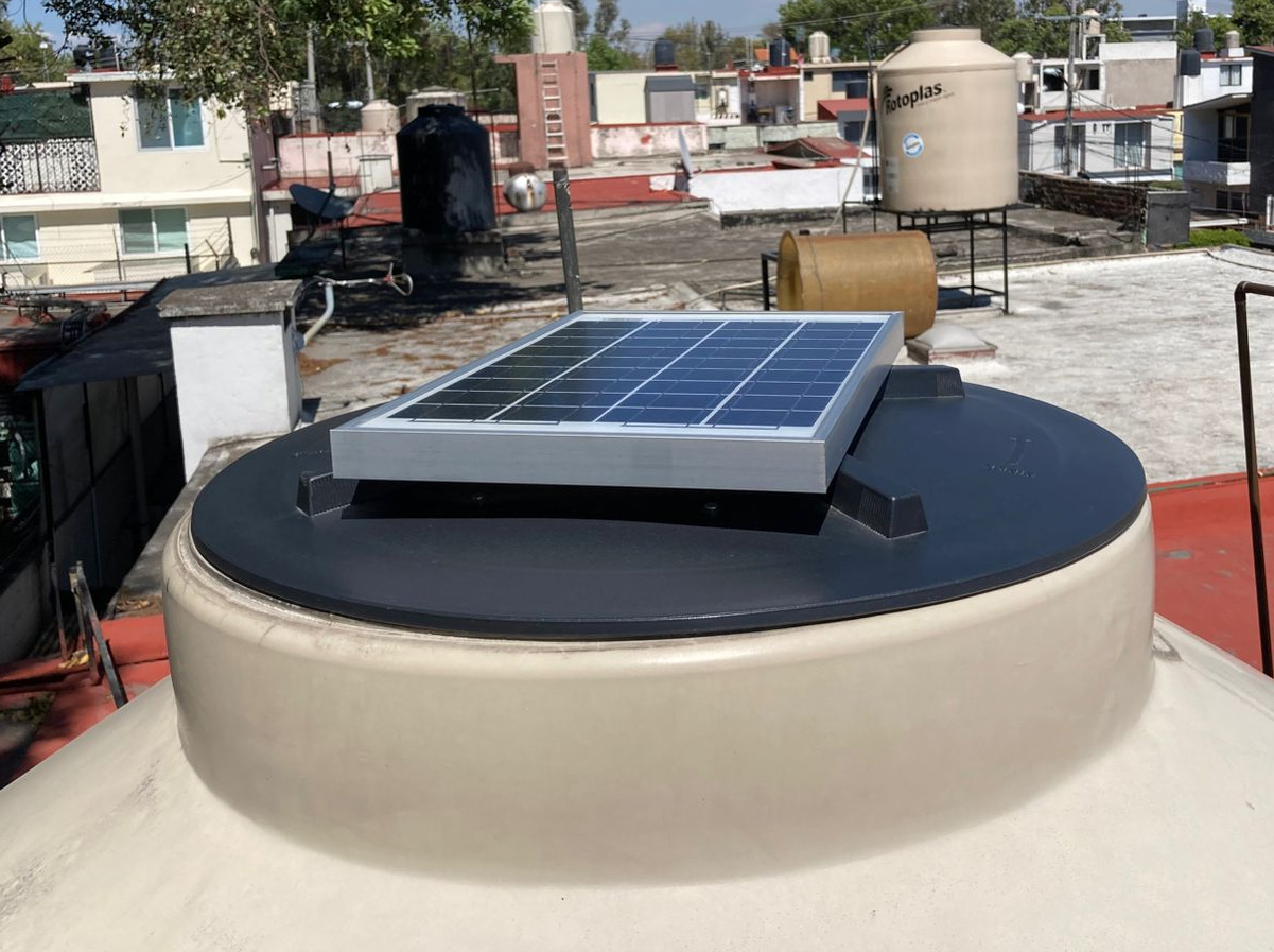 Small solar panel on top of a water tank on a rooftop, with urban buildings in the background.