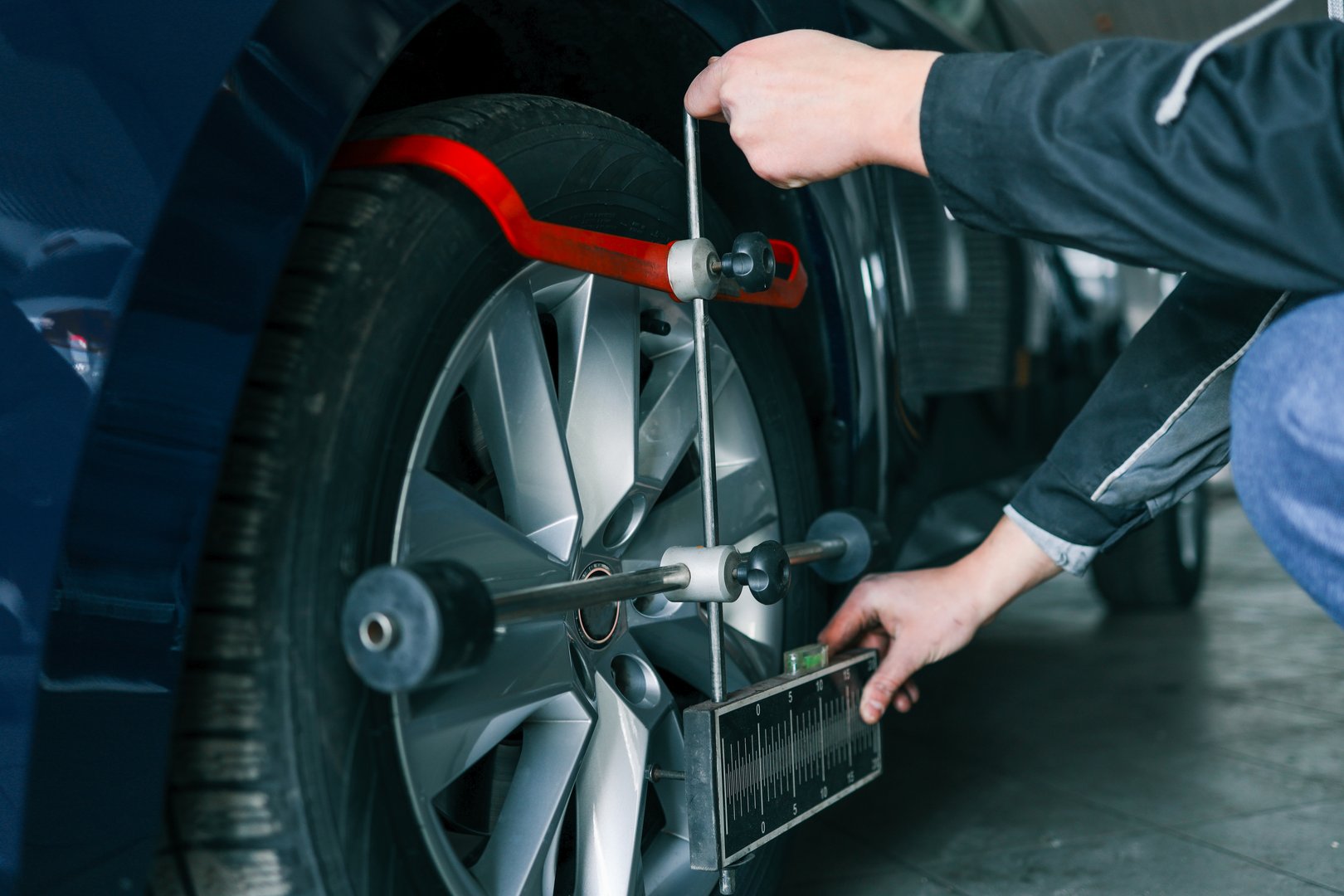 Mechanic adjusting a car's wheel alignment using a professional measuring tool in an auto repair shop. Close-up on the wheel and equipment.
