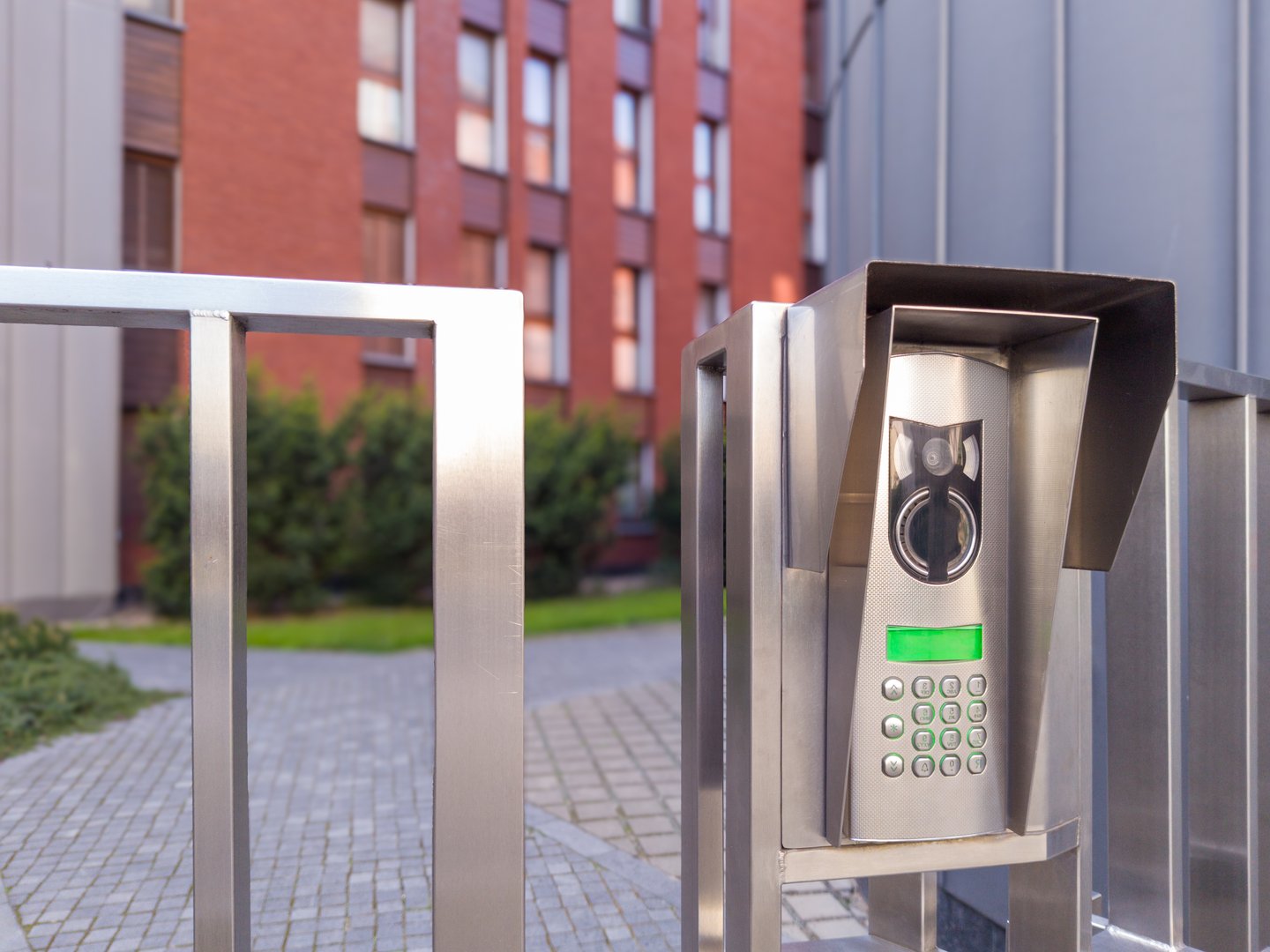 Video intercom with numeric keypad and camera installed on a stainless steel gate at a modern residential complex