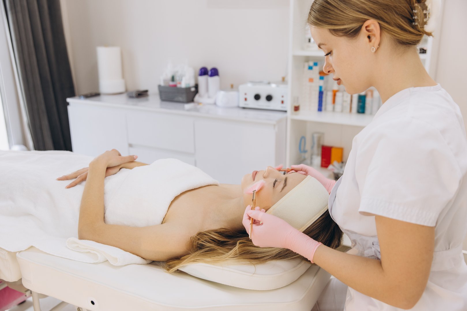 Professional beautician applying facial skincare treatment on relaxed client during spa session