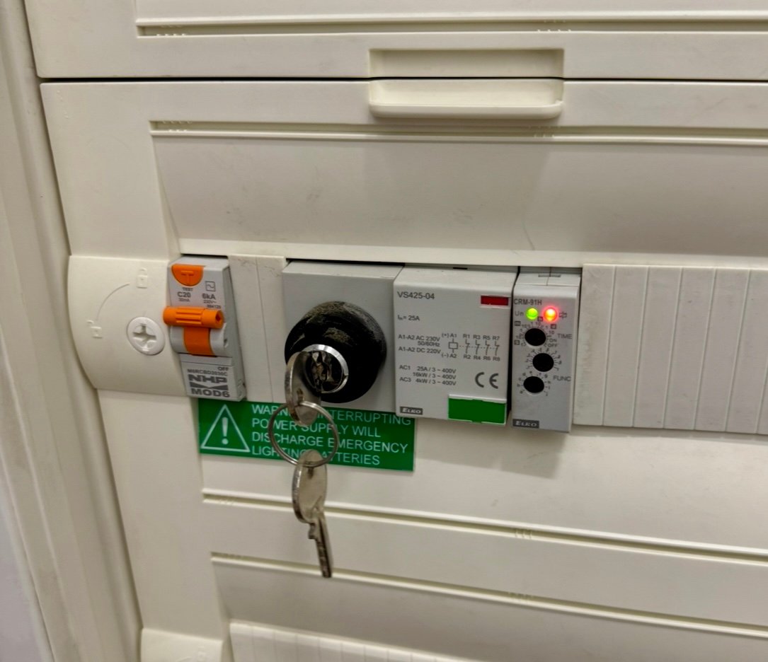 Industry-standard illuminated Fire Exit sign seen at the fire escape and emergency exit doors within a typical hospital. An alarm system can be seen in the background.