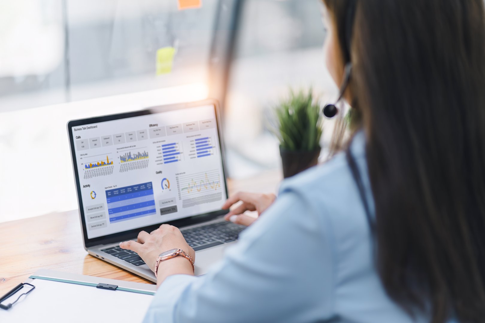 Operator wearing a headset, using a dashboard on laptop for data analysis in modern office
