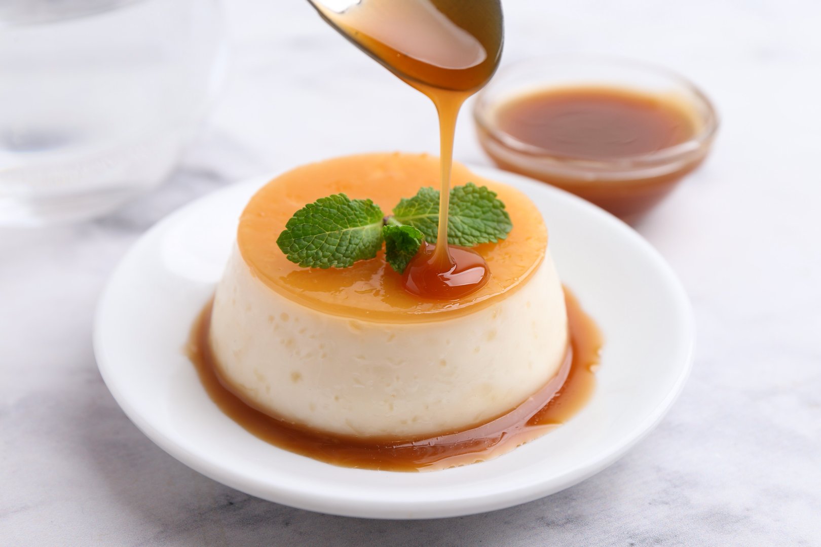 Tasty pudding with caramel sauce served on white marble table, closeup
