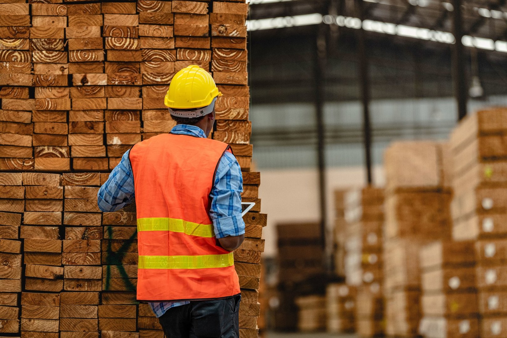 African worker carpenter wearing safety uniform and hard hat working and checking the quality of wooden products at workshop manufacturing. man and woman workers wood in dark warehouse industry.