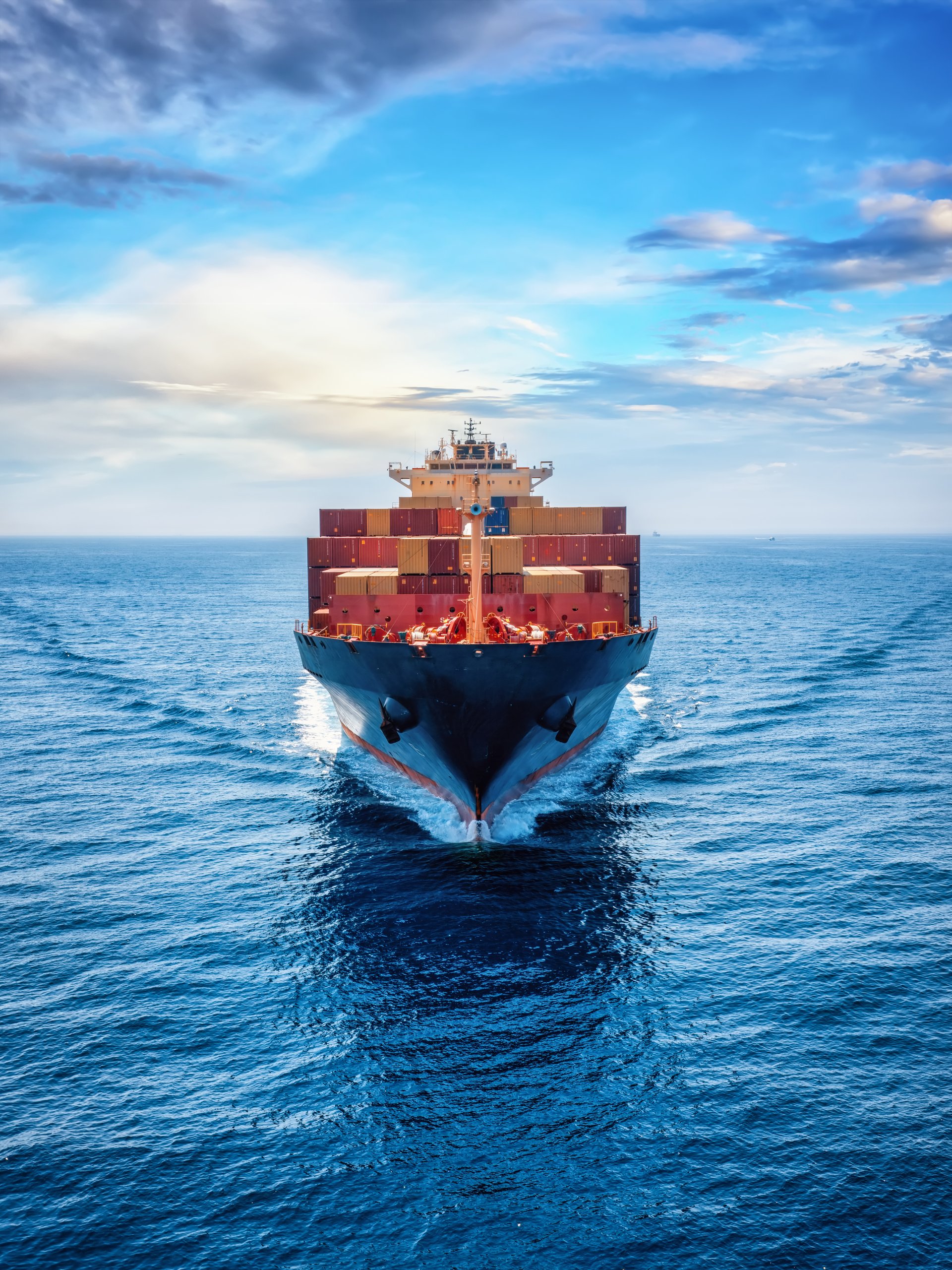 Front view of a loaded container cargo vessel traveling over calm ocean with speed