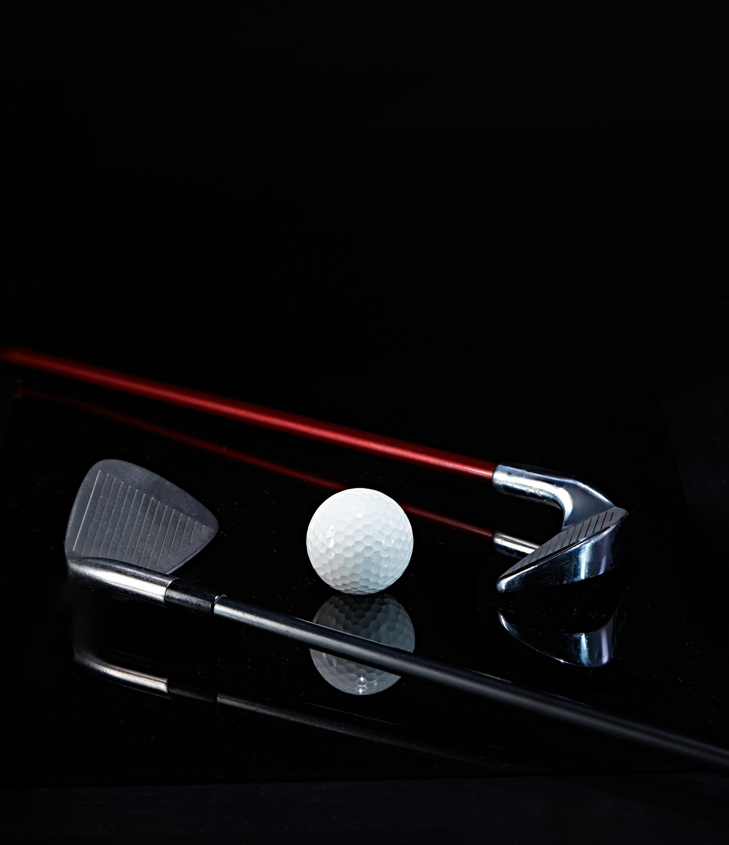 golf club and golf ball photographed against a dark background with reflections in the photo