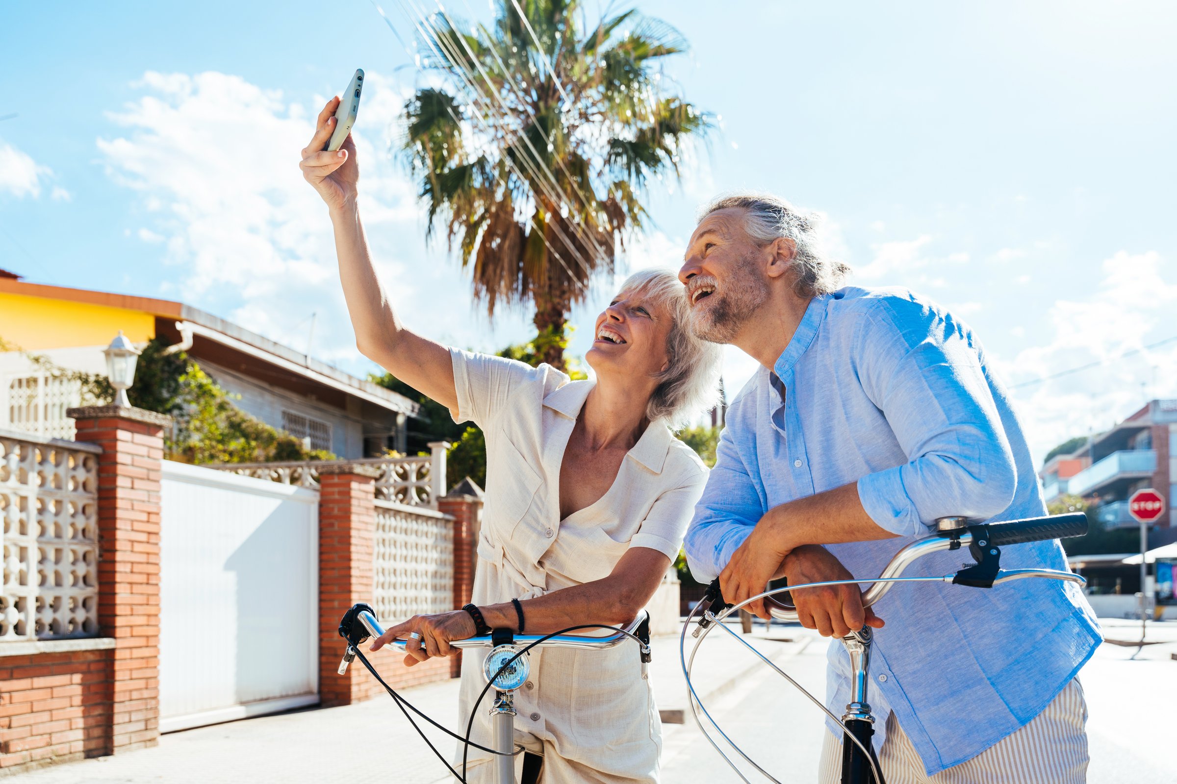 Beautiful happy senior couple dating at the seaside during summertime - Mature married couple in love bonding outdoors and riding bicycle, concepts about elderly lifestyle, transportation and quality of life