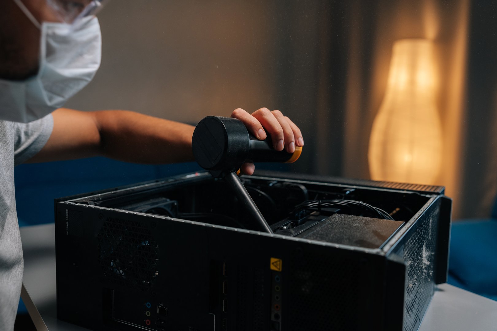 Closeup of technician in face mask and safety glasses cleaning computer case using small vacuum cleaner, demonstrating proper maintenance procedures. Concept of service, repair and cleaning computer