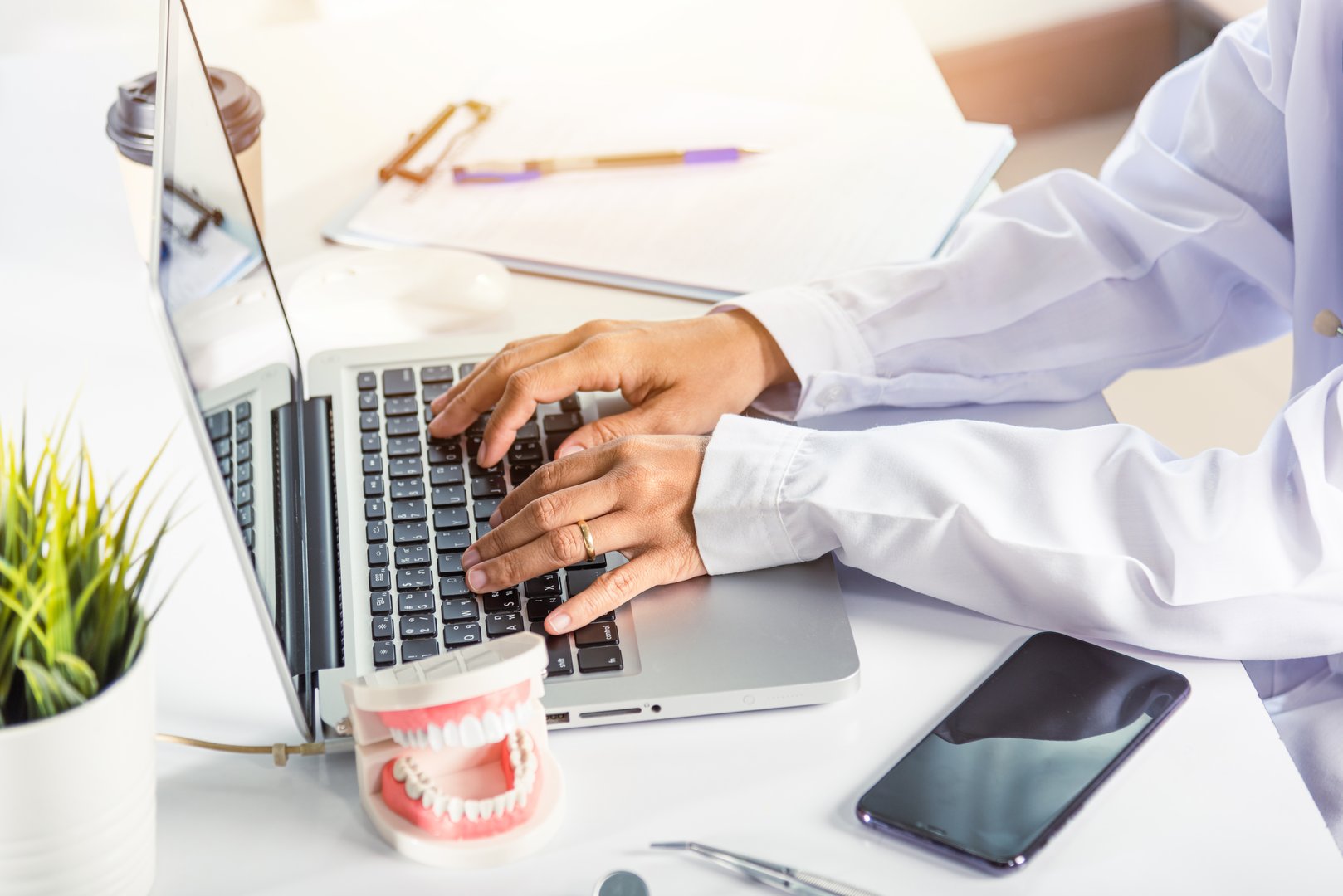 Dentist doctor or nurse in uniform use oral software teeth Xray and typing information medical history form into laptop computer for record document report, tooth model on desk, dentistry concept