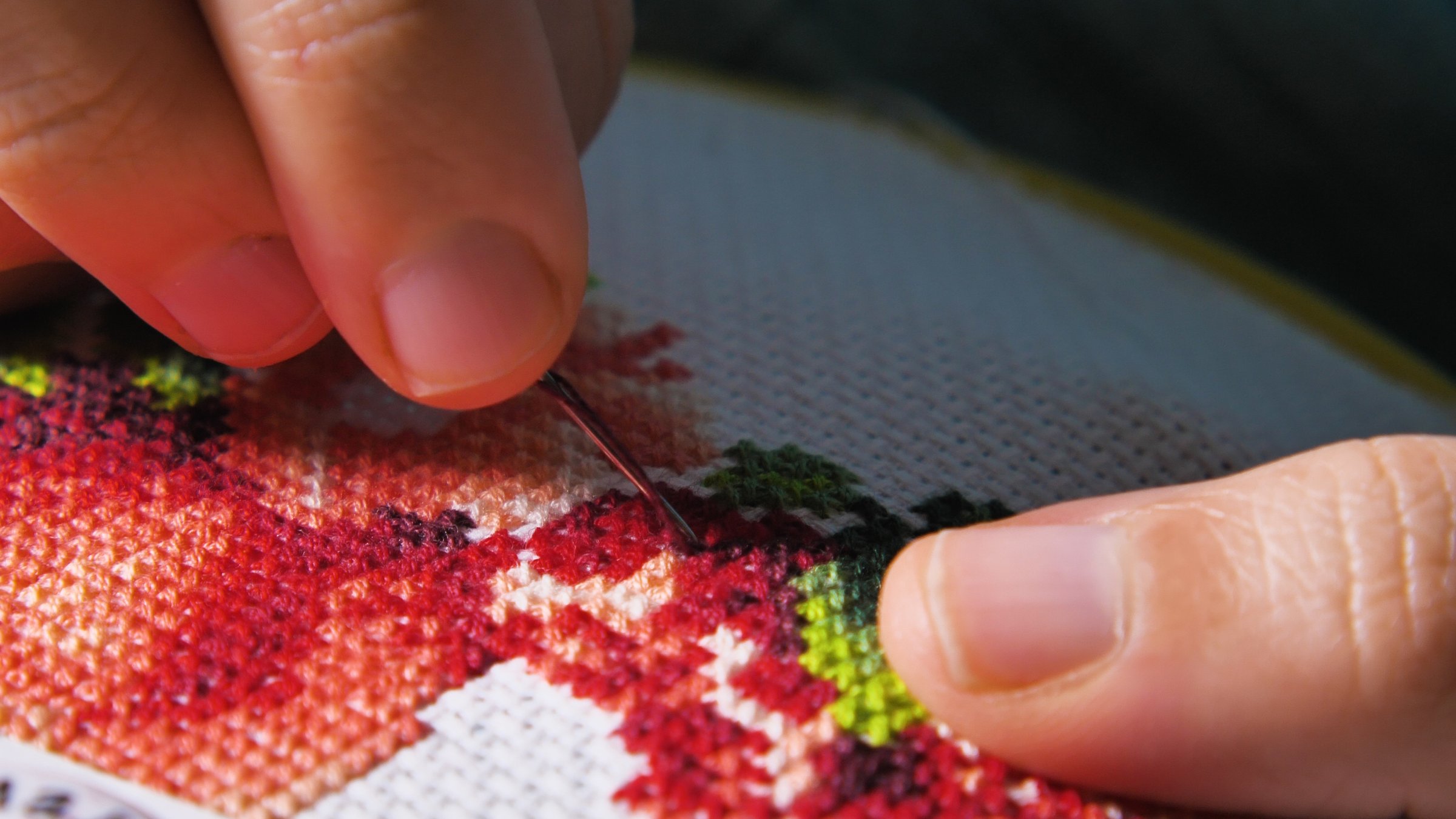 A close-up of hands doing cross stitch embroidery with colorful threads