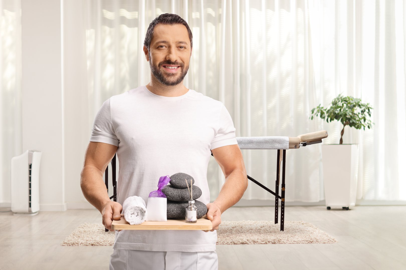 Massage male therapist holding a towel and stones on a board