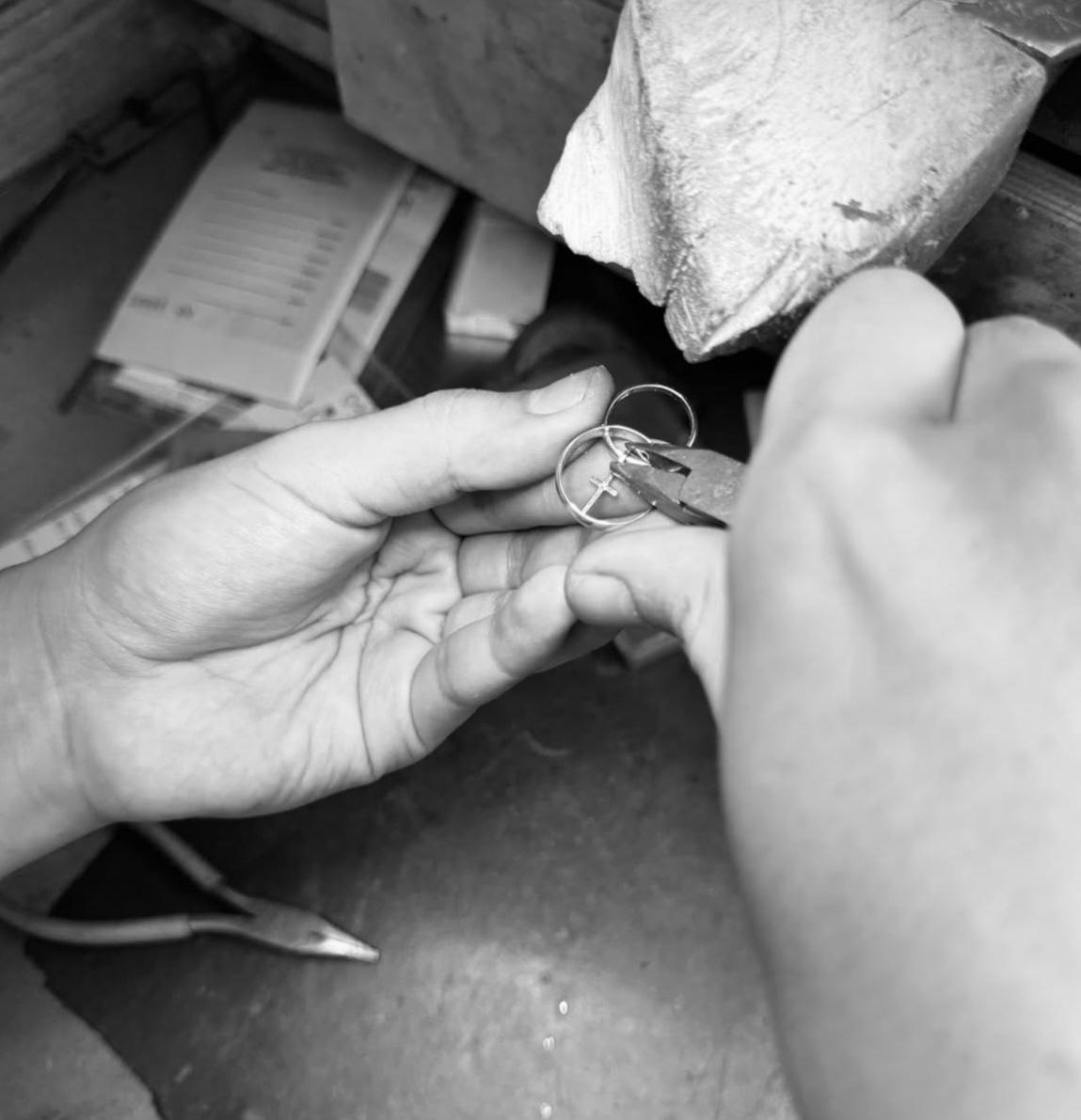 Person using pliers to craft or repair a ring at a workbench, with tools and materials visible in the background.