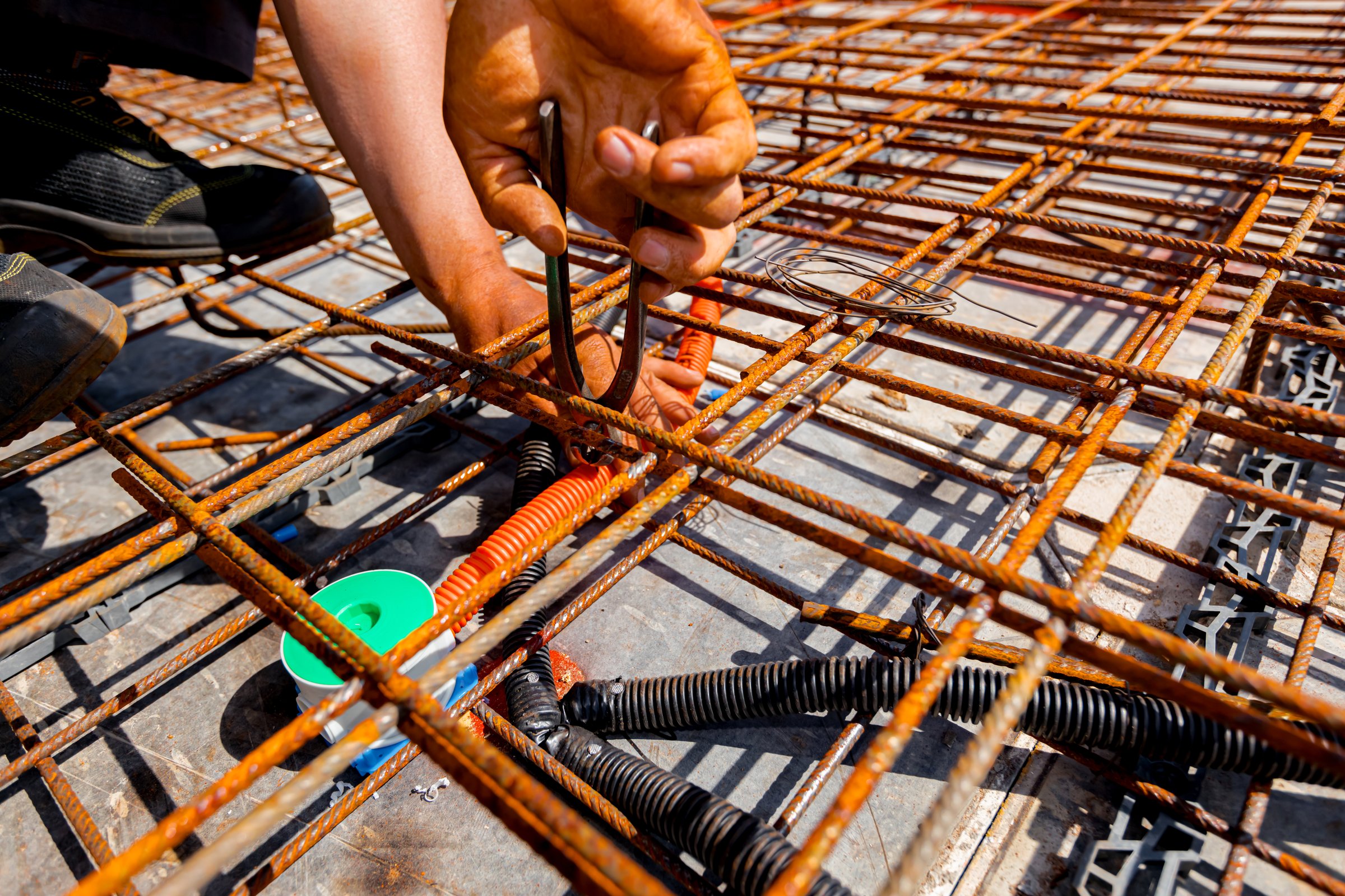Worker's hands as he assembly protective ribbed plastic hoses, for cables, placing and connect them to distribution box, under rusty rebar, prepared for pouring concrete over them.
