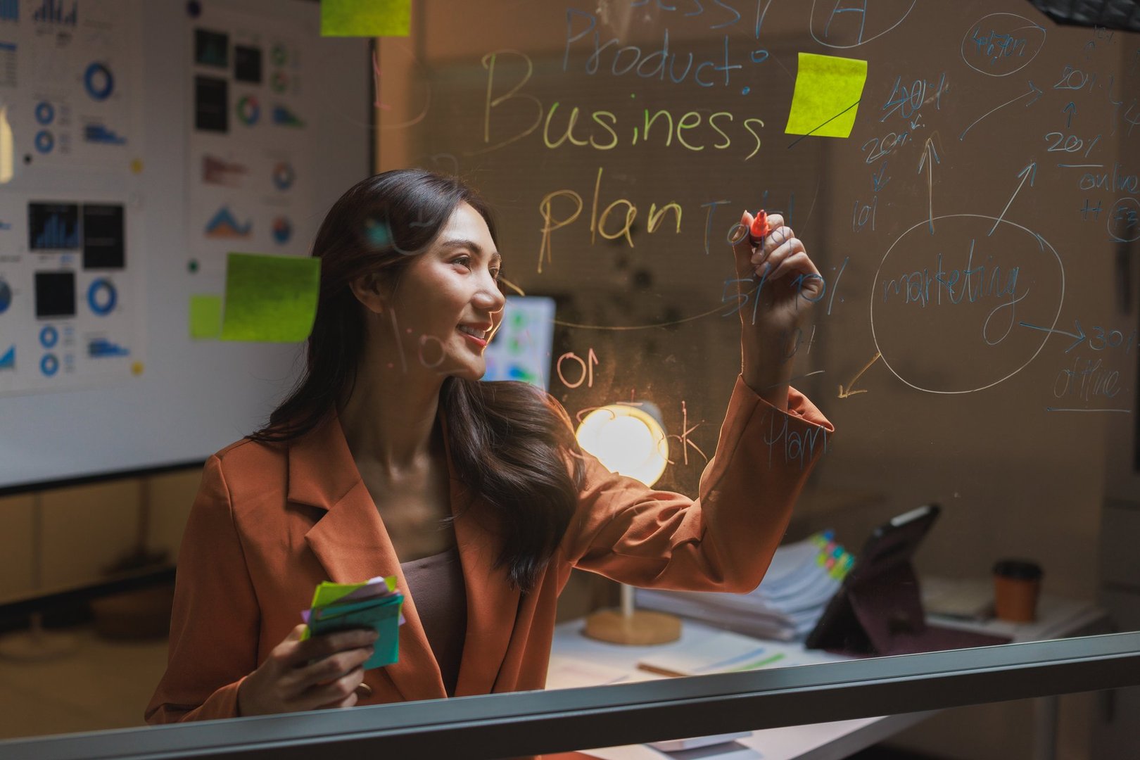 Woman writing business plan ideas and marketing strategy on a clear glass board
