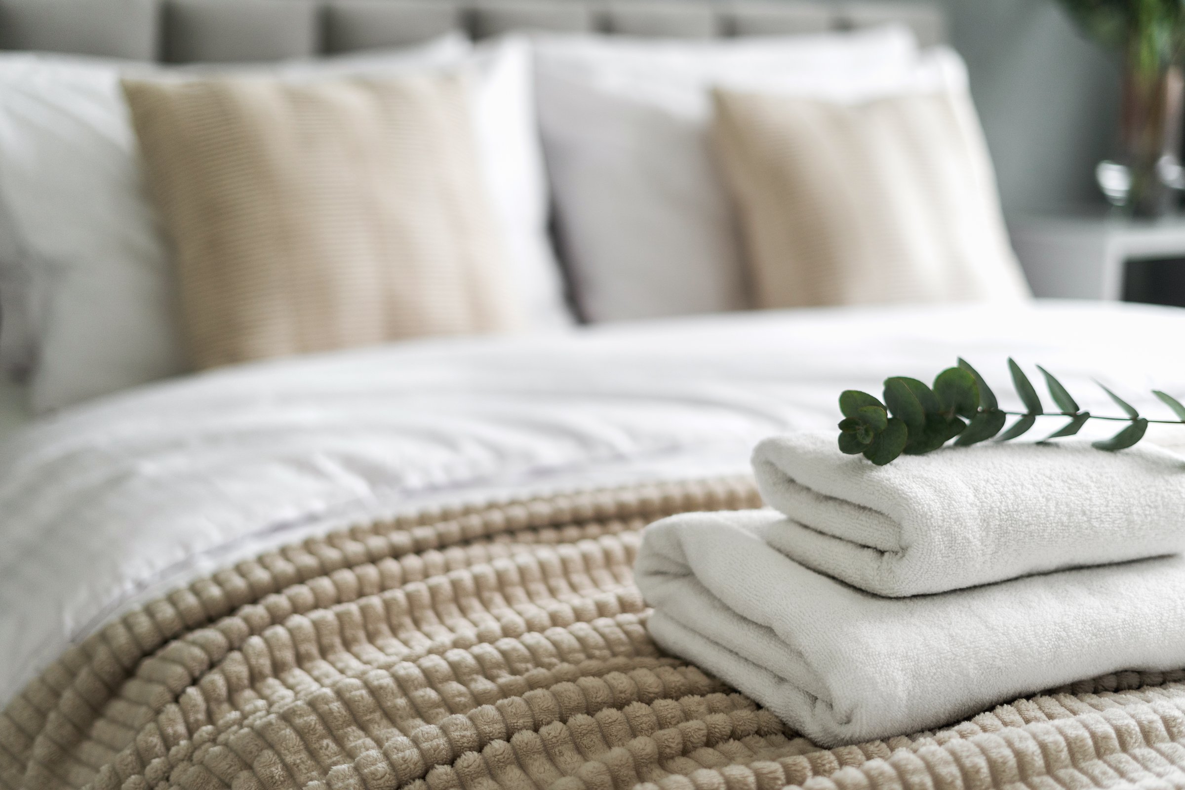 Freshly folded white towels arranged neatly on a hotel bed, ready for guests to use during their stay. Bathroom textile in cozy bedroom interior against decorative cushion and pillows, selective focus