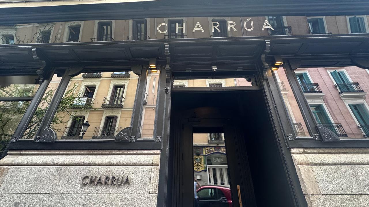 Exterior of a building with the name CHARRÚA displayed above the entrance. Reflections of nearby buildings on the glass.