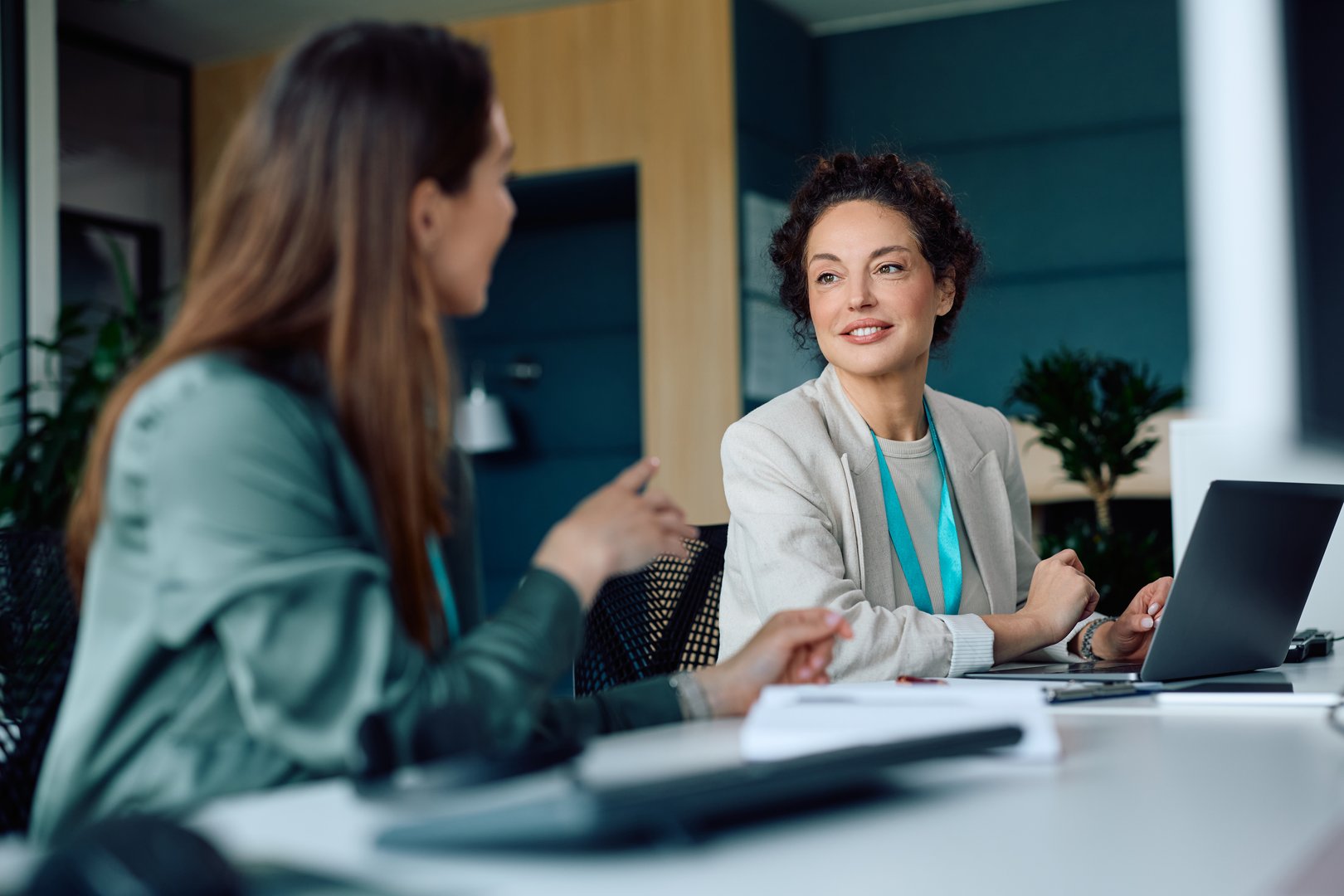 Mature businesswoman working on a computer while talking to female coworker at corporate office.