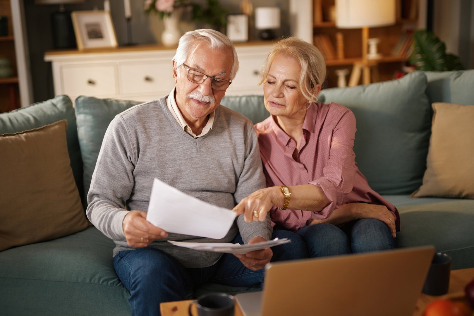 Senior couple reviewing paperwork and using laptop, planning their retirement finances and life insurance at home
