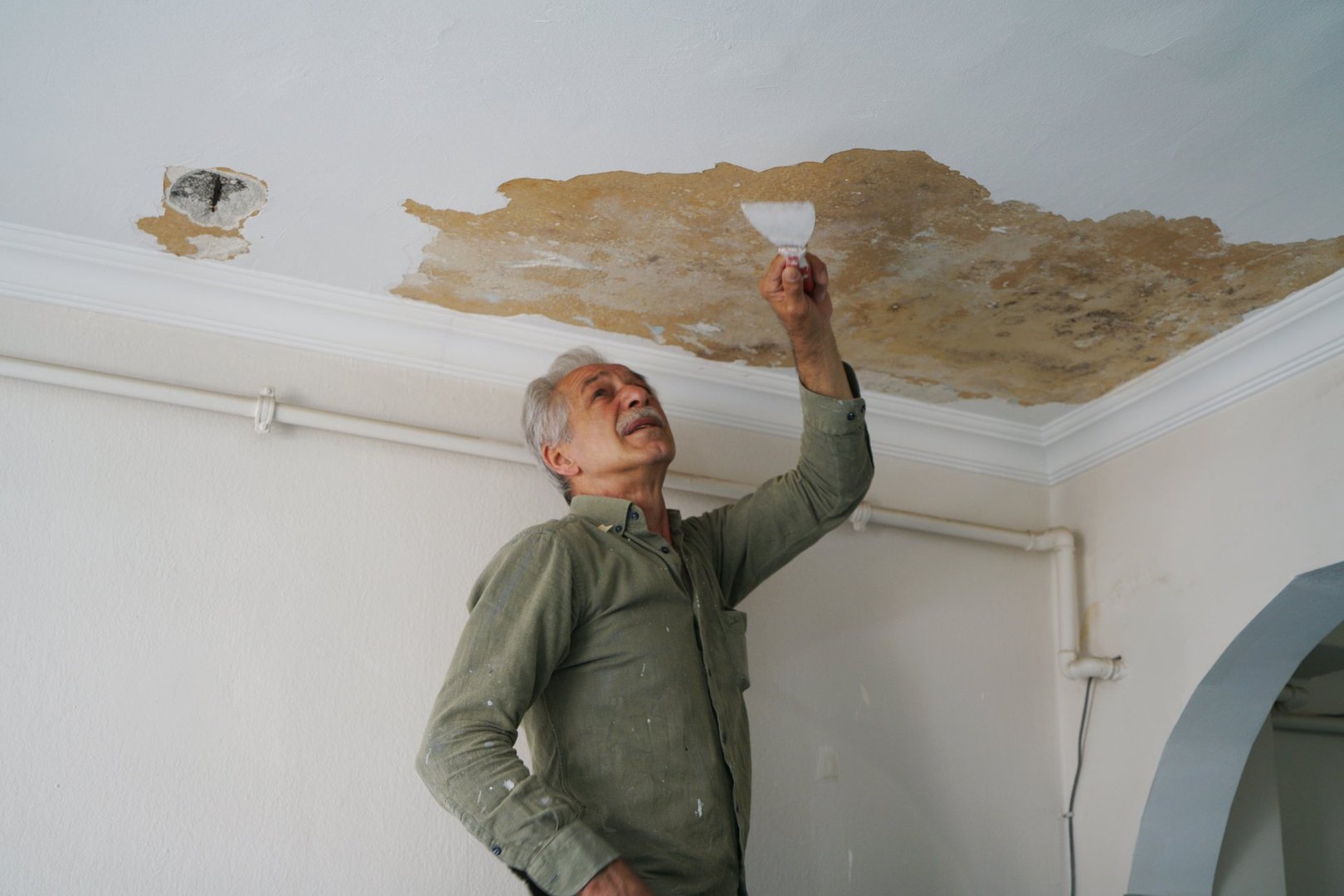 Scraping the wall with a metal trowel, preparing the surface for painting. Solving moisture problems. Home maintenance and renovation.