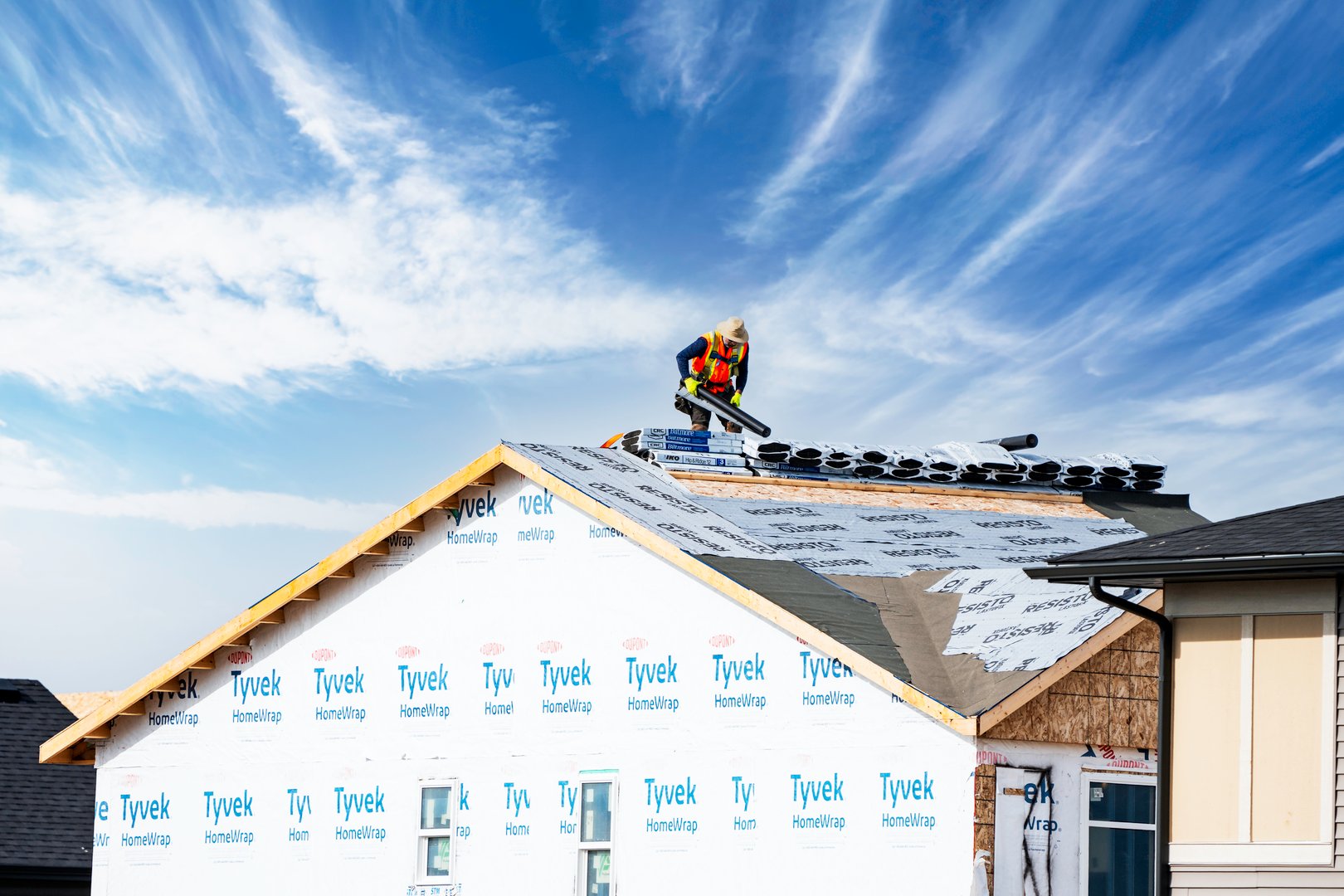 Airdrie Alberta Canada, May 21 2024: Roofer at work on a new home under construction with shingles and supplies.