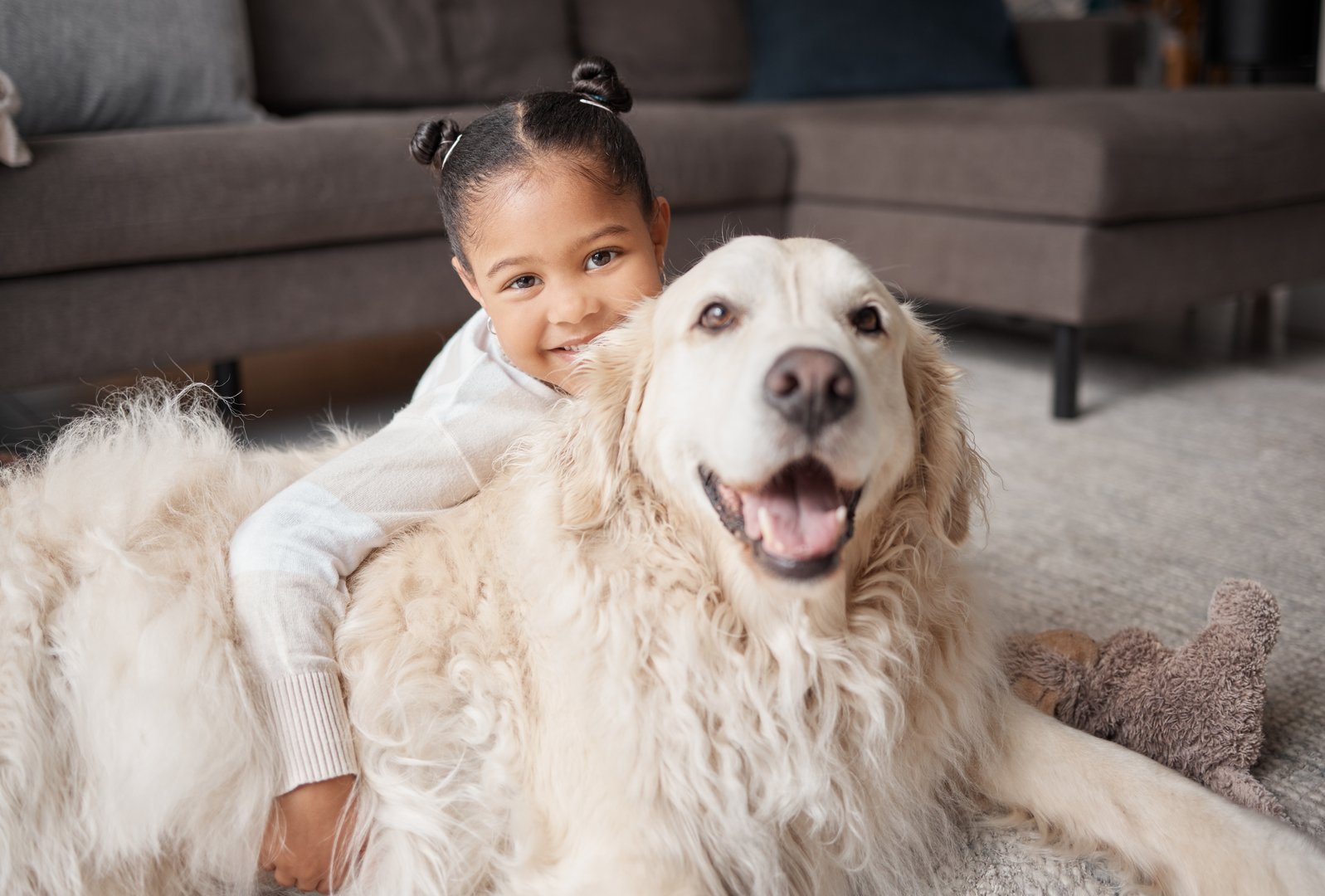 Portrait of a cute little girl holding her emotional support dog while bonding on the lounge floor. A mixed race child looking happy and safe with her puppy at home