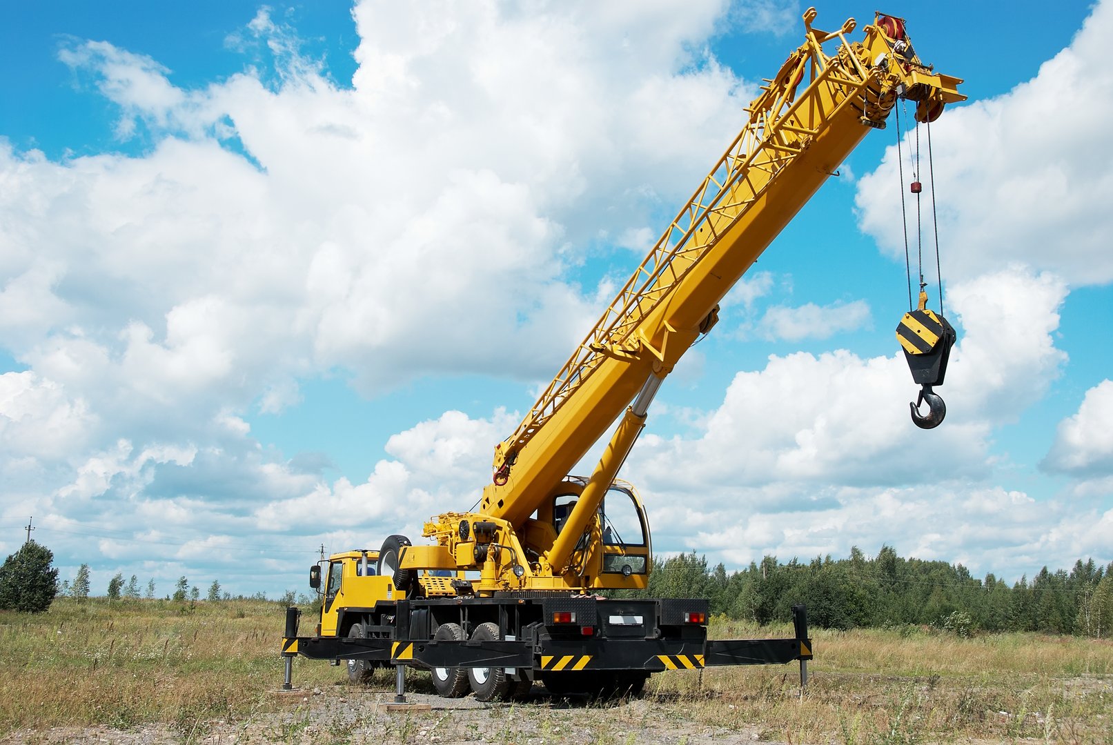 yellow automobile crane with risen telescopic boom outdoors over blue sky