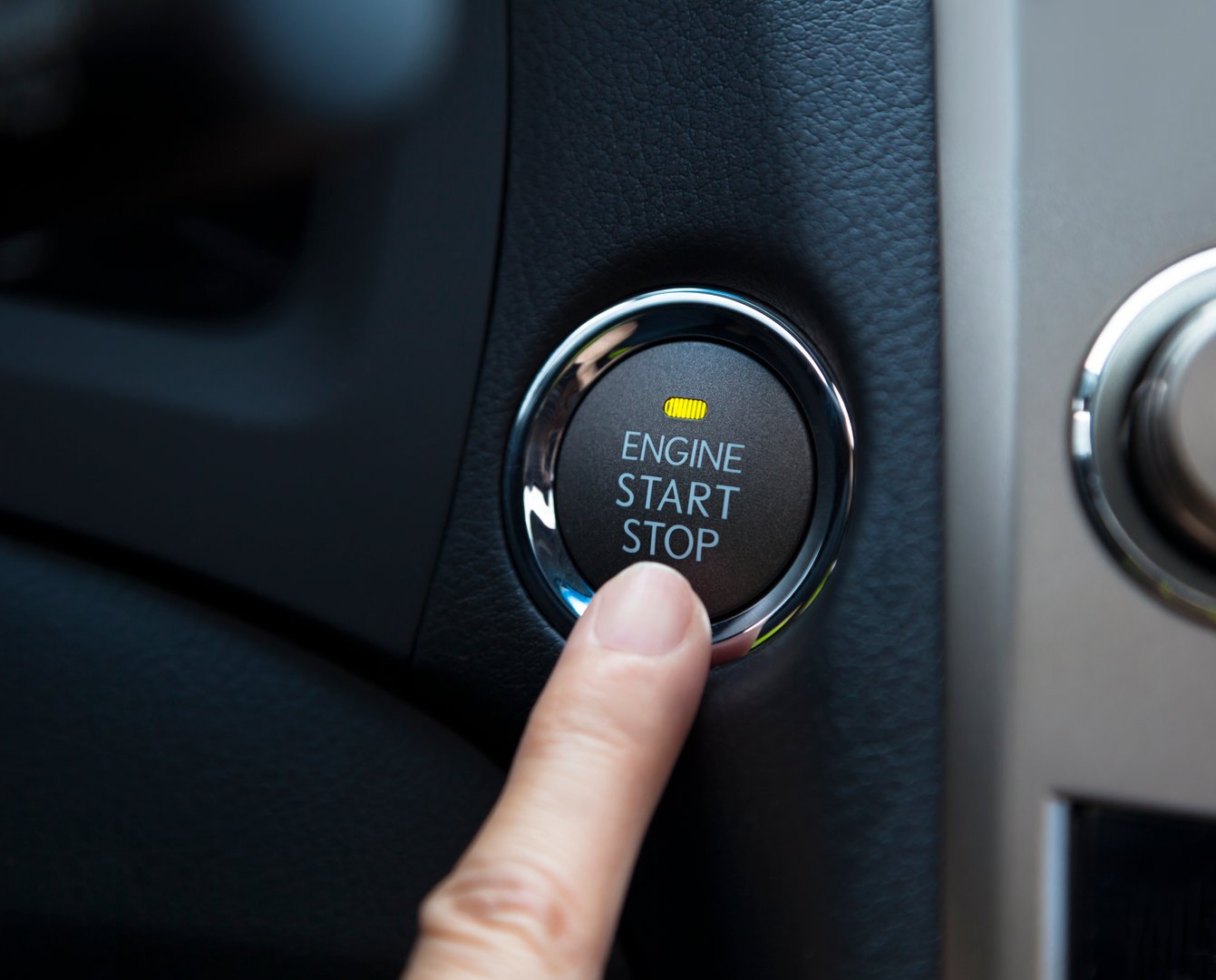 finger pressing the Engine start stop button of a car
