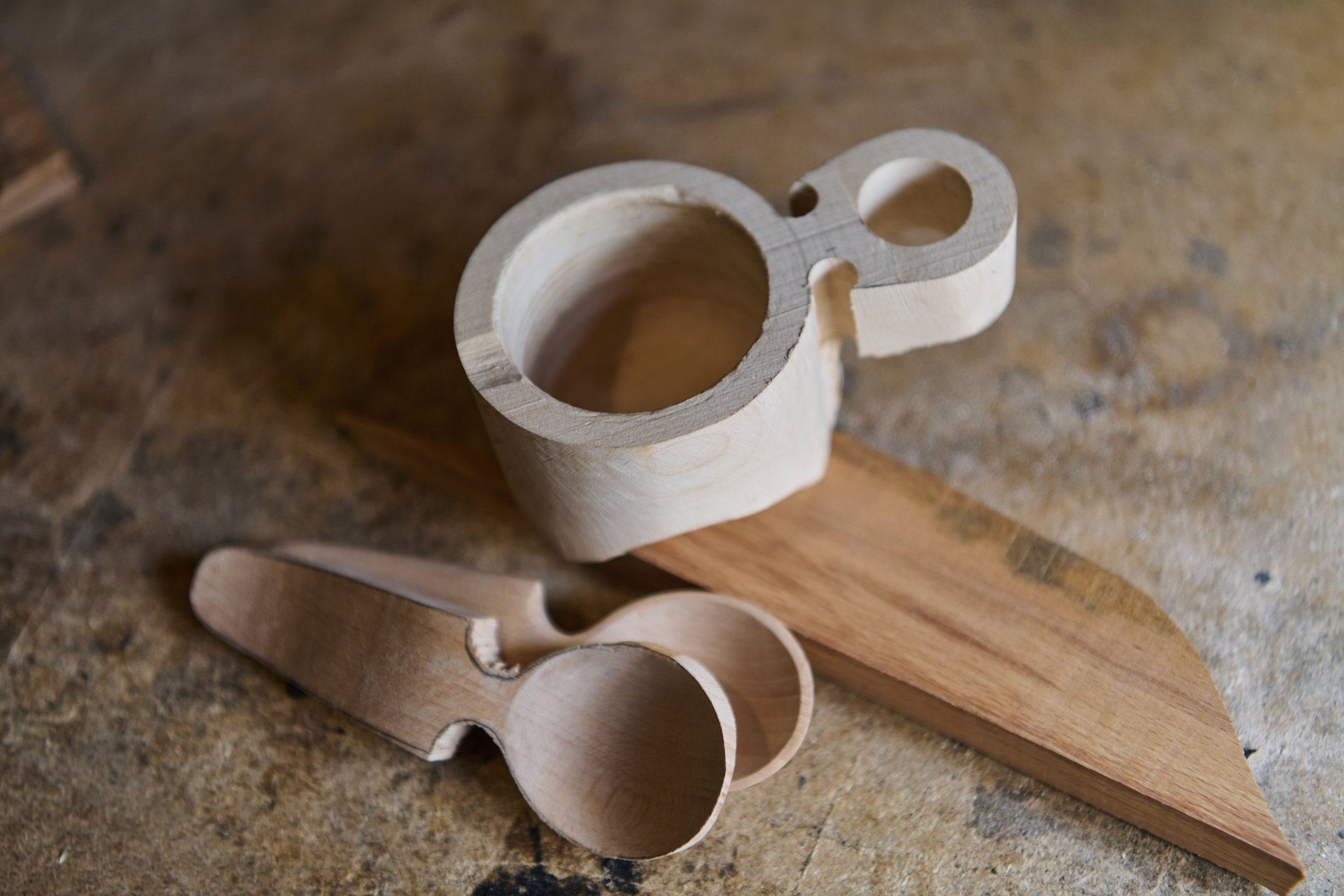 Close-up of a handcrafted wooden Kuksa cup and spoons, showcasing unfinished wood carving. Perfect for illustrating traditional Finnish craftsmanship, woodworking projects, and rustic design elements.