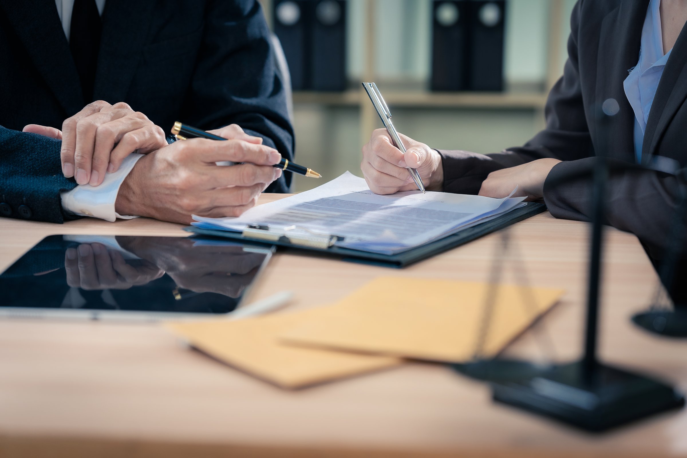 Law office with legal books and scales on table. Legal consultation: lawyer and client reviewing documents together. Representing trusts and legal proceedings. Close-up.