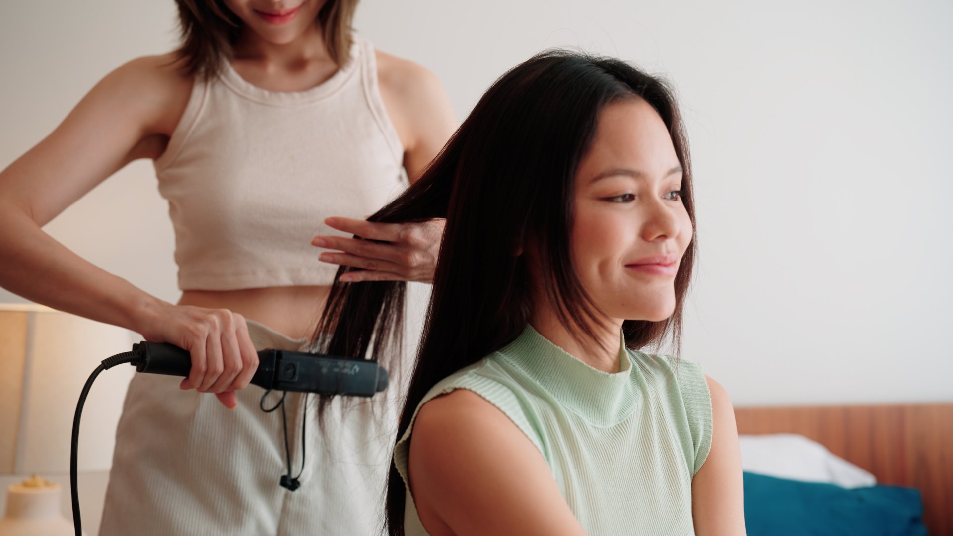 Two female friends styling hair with a hair straightener.