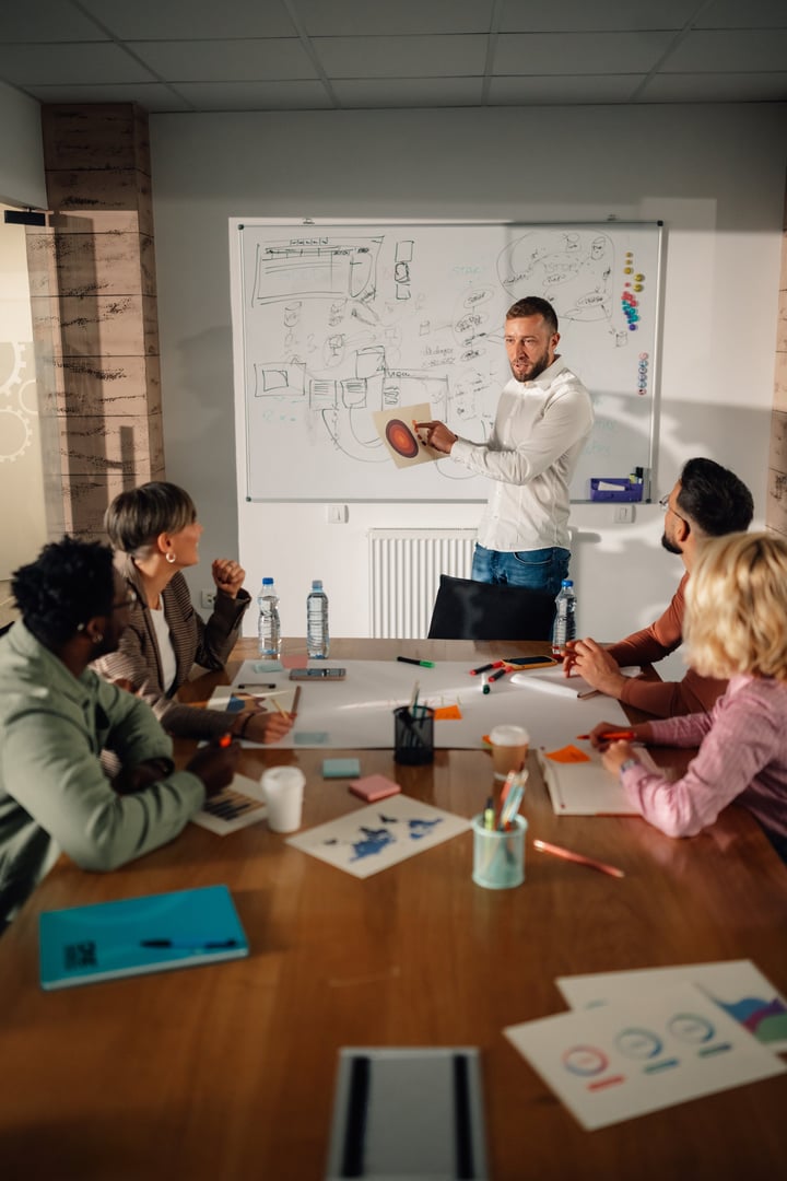 Marketing team is having a brainstorming session in a modern office, analyzing diagrams and charts while a project manager explains a new strategy