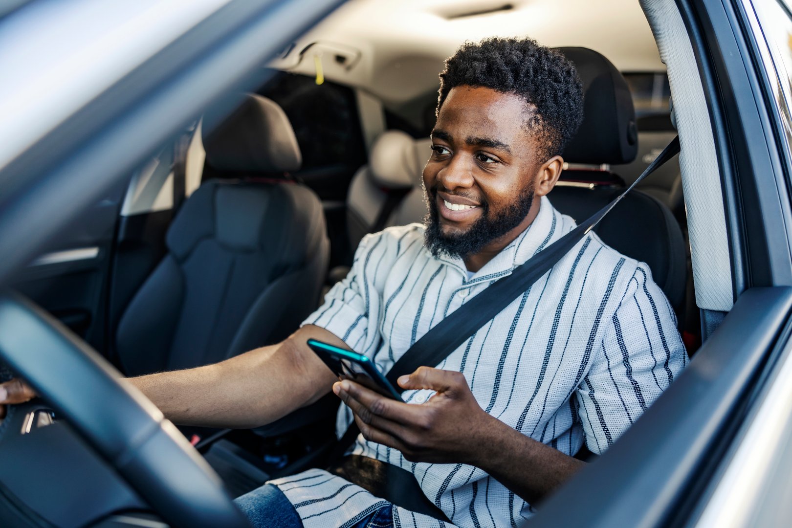 Portrait of a black driver driving his car and typing directions in cellphone on GPS