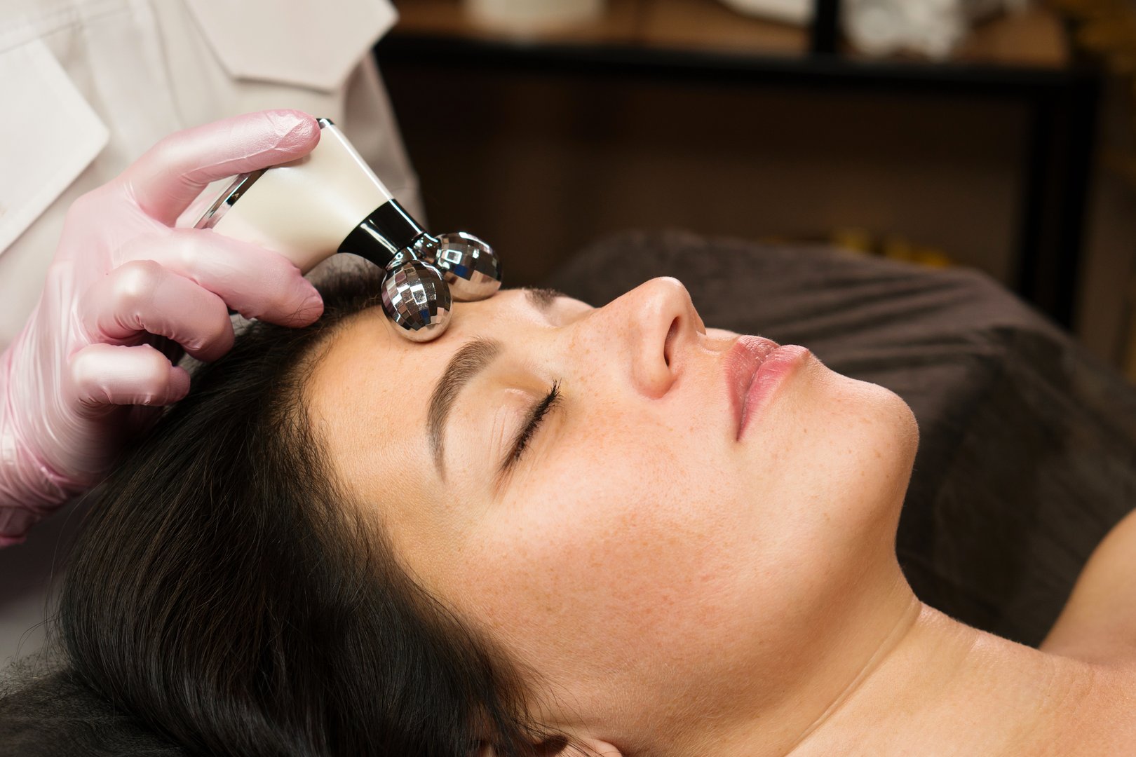 A cosmetologist uses a microcurrent massager on a clientâs forehead for skin tightening.