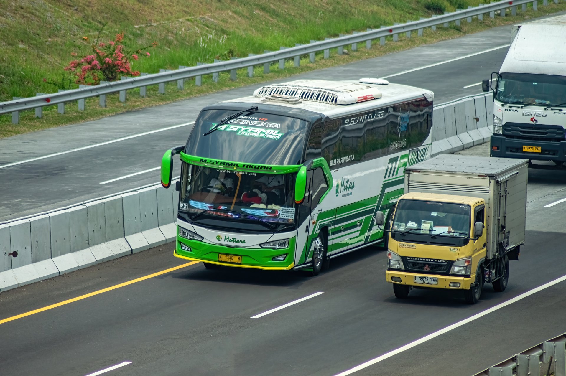 A green and white bus travels on a toll road alongside trucks, highlighting transportation infrastructure. Ideal for articles on transportation and travel. Indonesia, 31 October 2024.