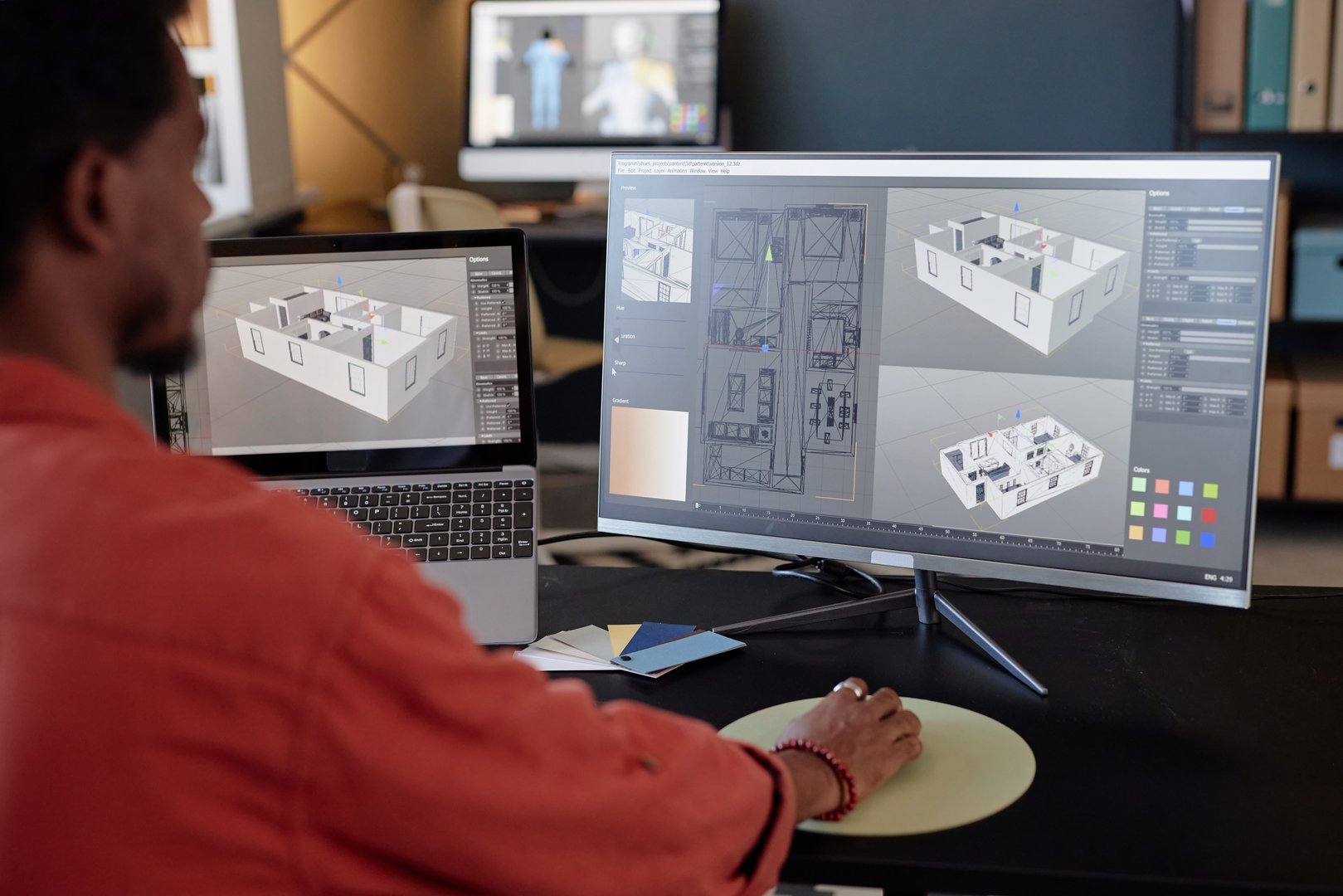 Person analyzing architectural designs on computer screens at office workspace, focusing on detailed models and layouts for a project. Engaging in work through high-end technology