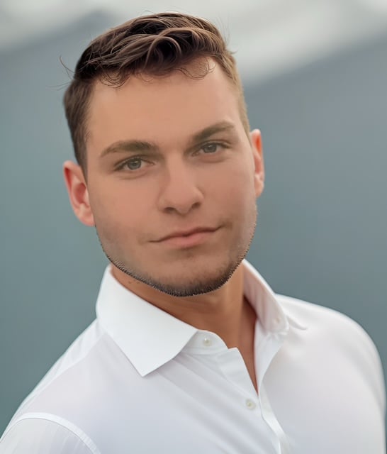 A man wearing a white shirt looking confidently at the camera. The background is blurred, highlighting the subject's face.