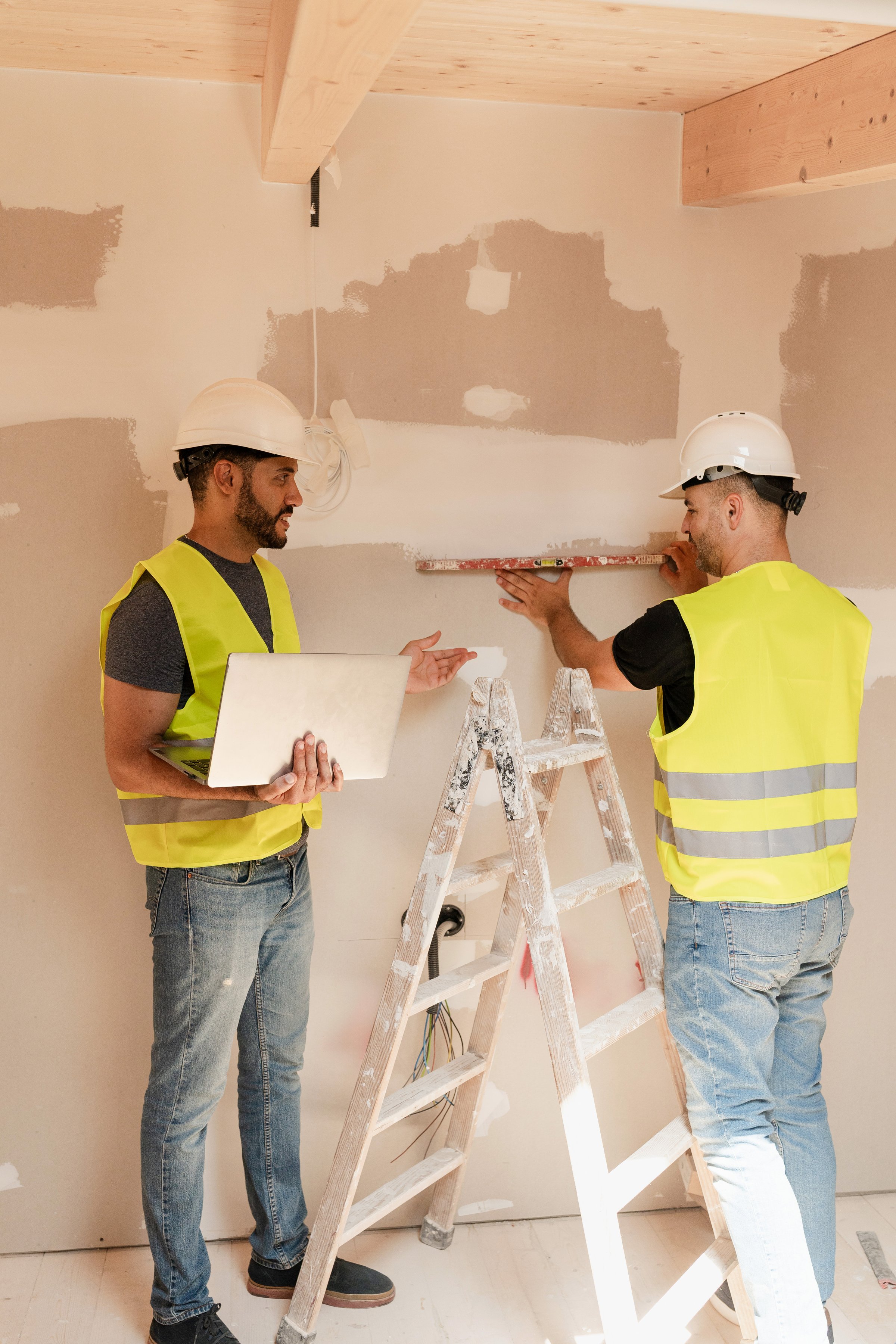 Two male Construction workers in safety vests leveling wall while working on a house renovation
