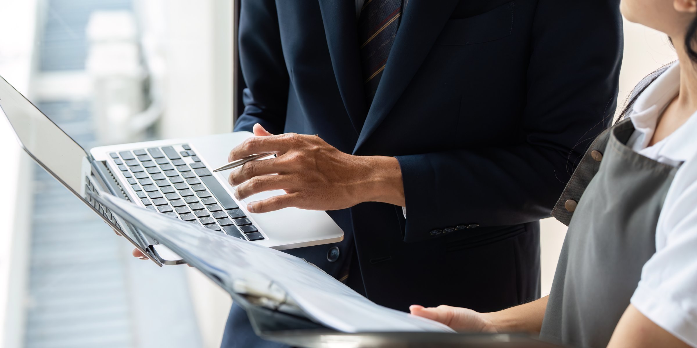 A close-up view of a businessman and a female employee analyzing data on a laptop in a bright office environment.