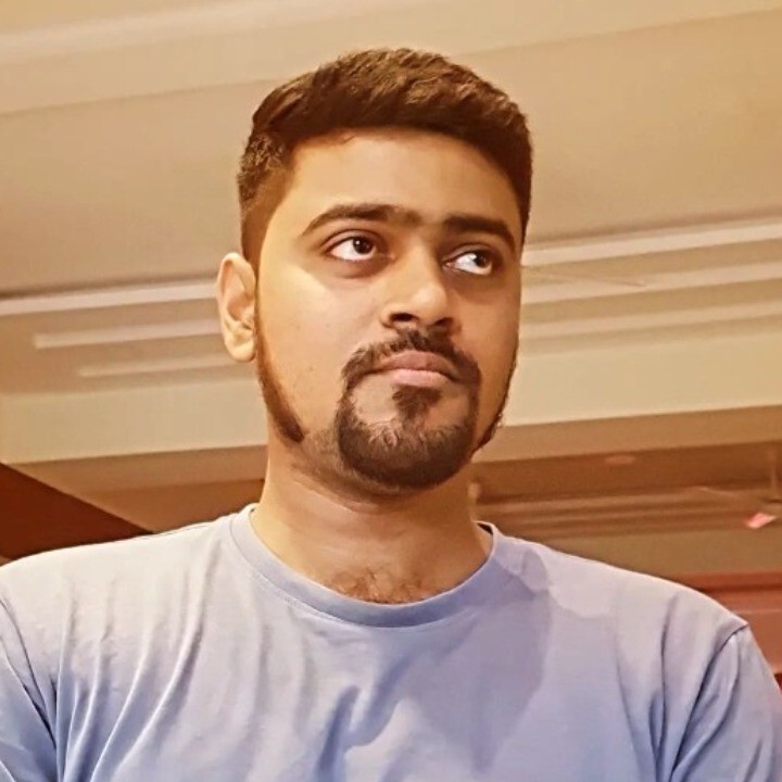 A man with short hair and a beard wearing a blue shirt, looking to the side in an indoor setting with soft lighting.