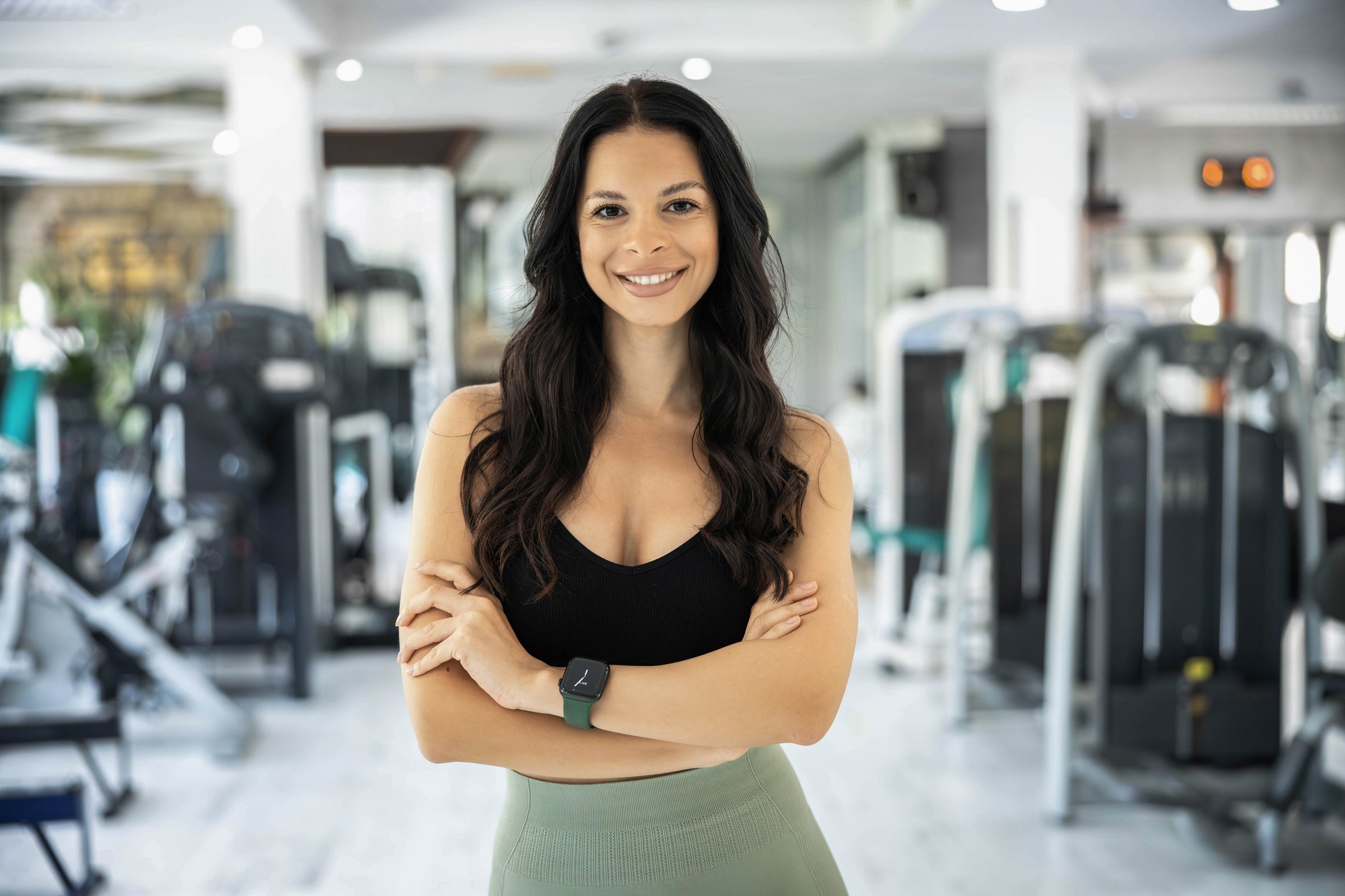 portrait of confident  sports woman smiling in a gym, showcasing her fitness expertise and the modern workout equipment behind her.